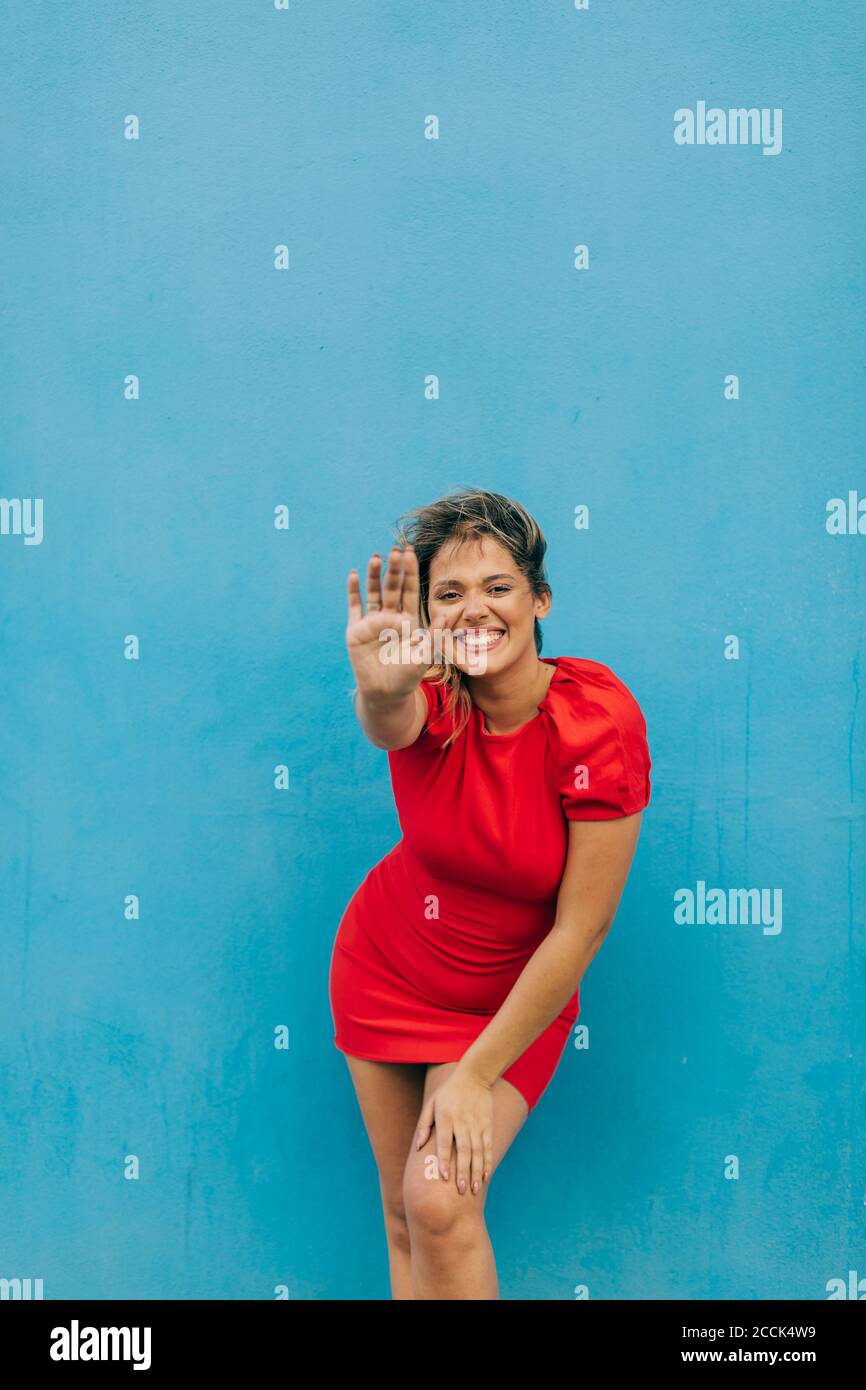 Lächelnde Frau mit Stop-Geste, während sie gegen die blaue Wand steht Stockfoto