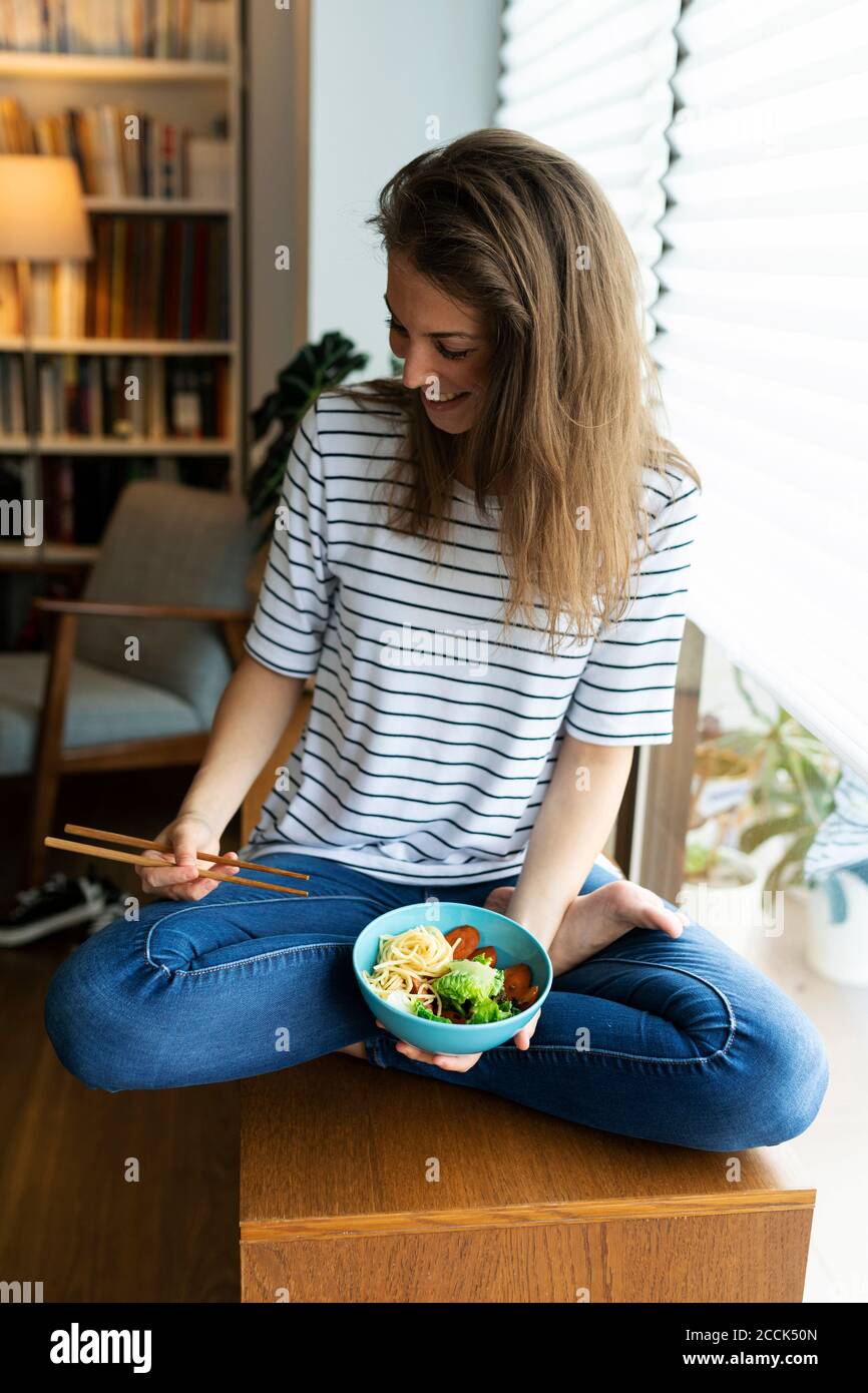 Lächelnde junge Frau mit Essen auf dem Tisch zu Hause sitzen Stockfoto