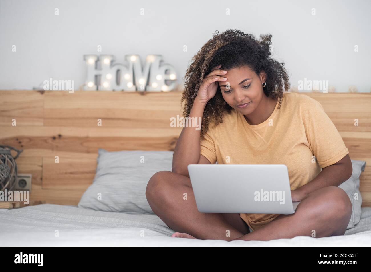 Junge Frau mit lockigen Haaren mit Laptop, während sie sitzt Bett Stockfoto
