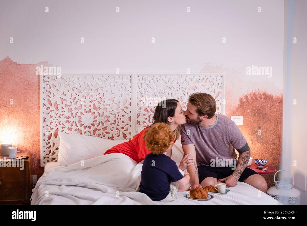 Eltern küssen beim Frühstück mit Sohn Bett zu Hause Stockfoto