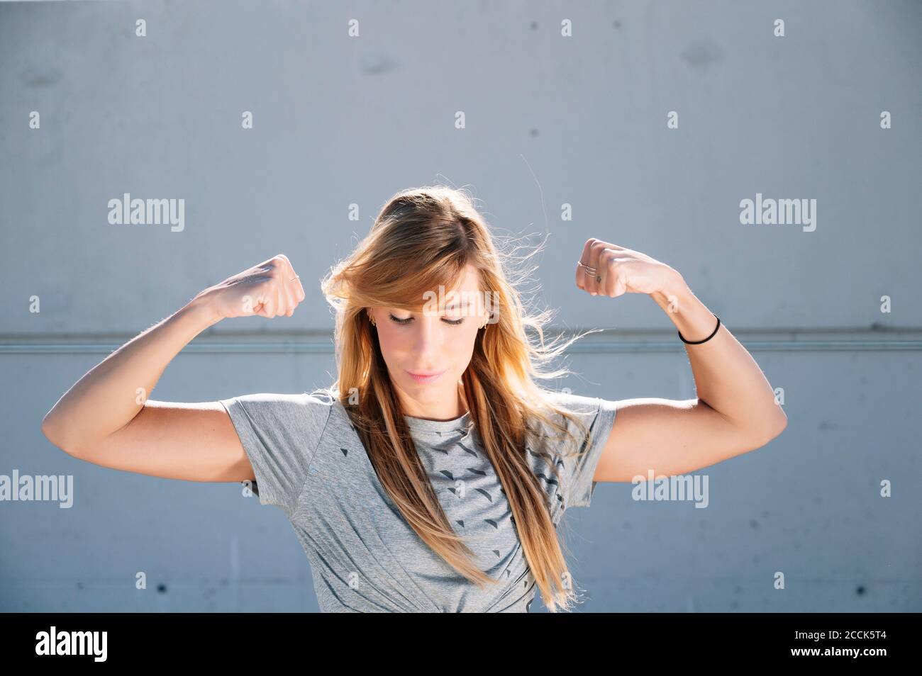 Selbstbewusste Frau, die Muskeln beugte, während sie in der Stadt gegen die Wand stand Stockfoto