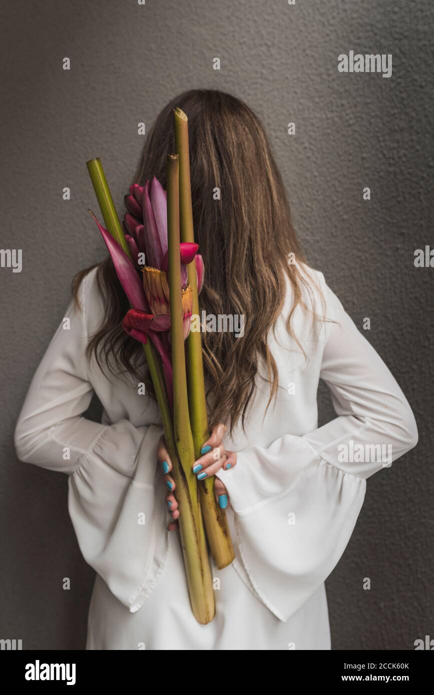 Frau mit braunem Haar hält Bouquet hinter Rücken an Wand Stockfoto