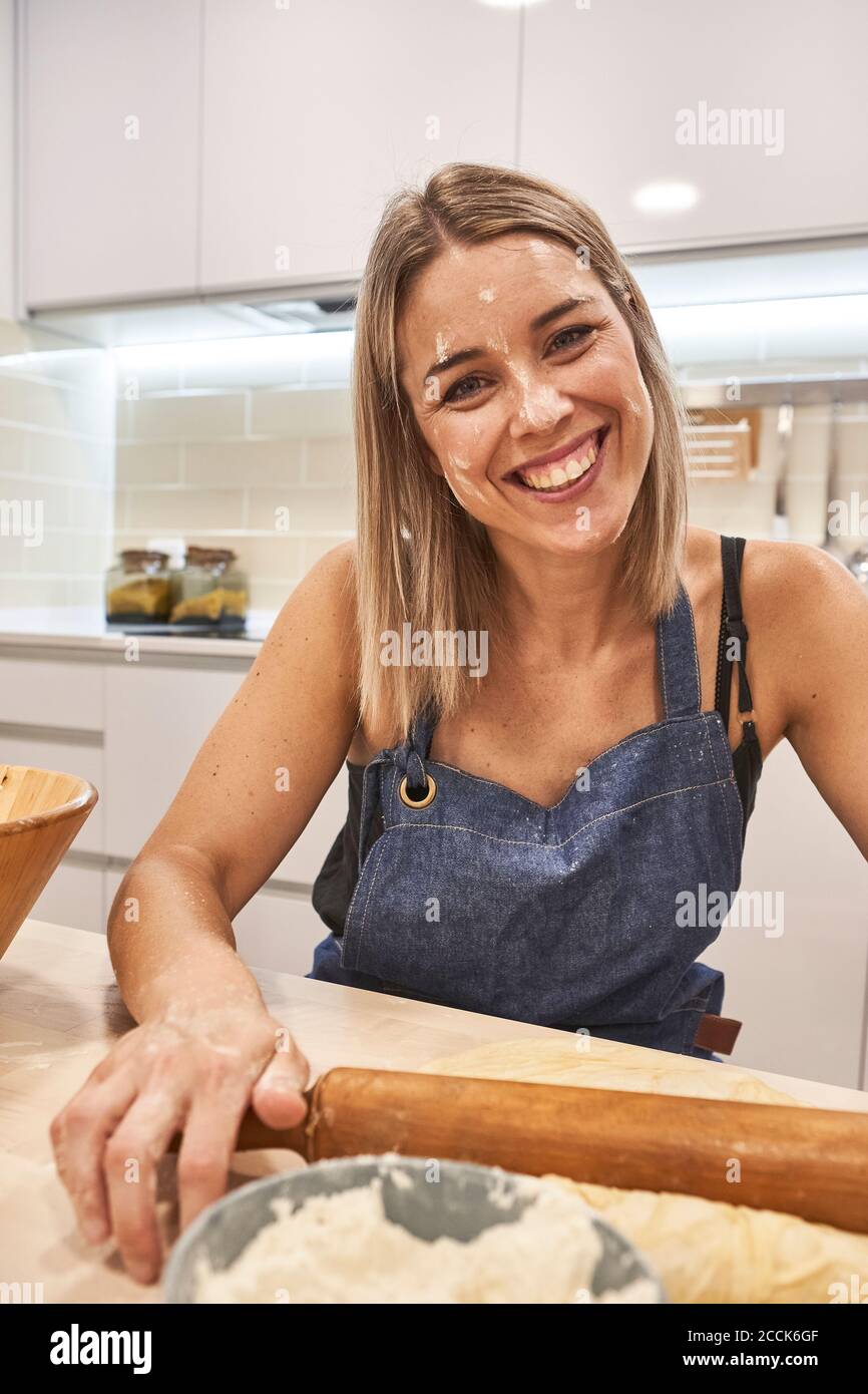 Nahaufnahme einer lächelnden Frau mit Mehl auf dem Gesicht, das Rollen hält PIN über Tisch in der Küche Stockfoto