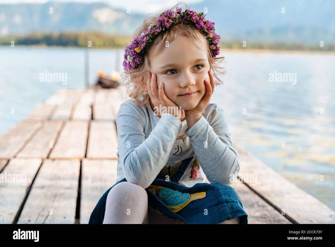 Nahaufnahme von niedlichen Mädchen trägt Tiara sitzen auf dem Steg gegen see Stockfoto