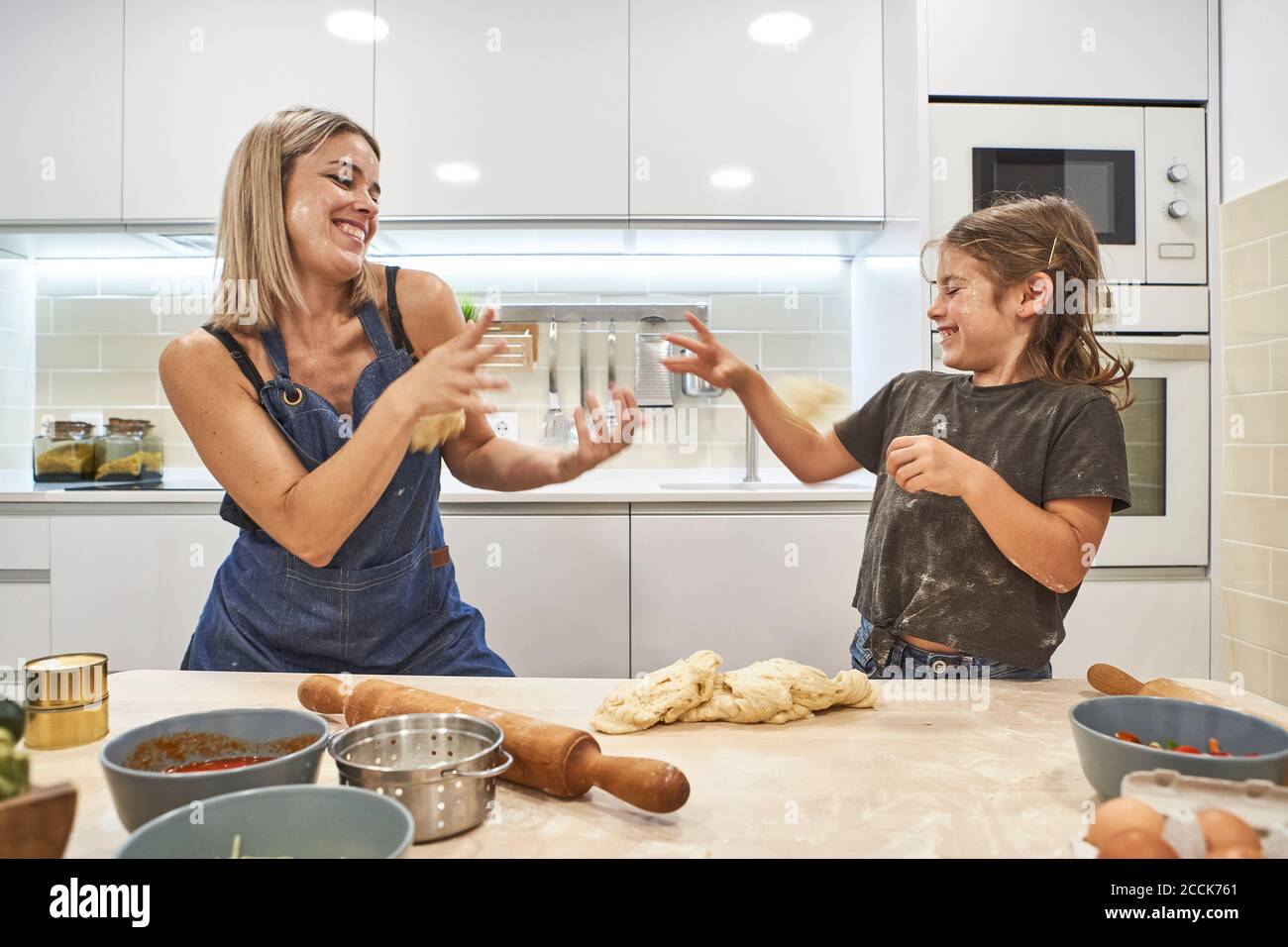 Fröhliche Mutter und Tochter spielen mit Pizzateig in der Küche Stockfoto