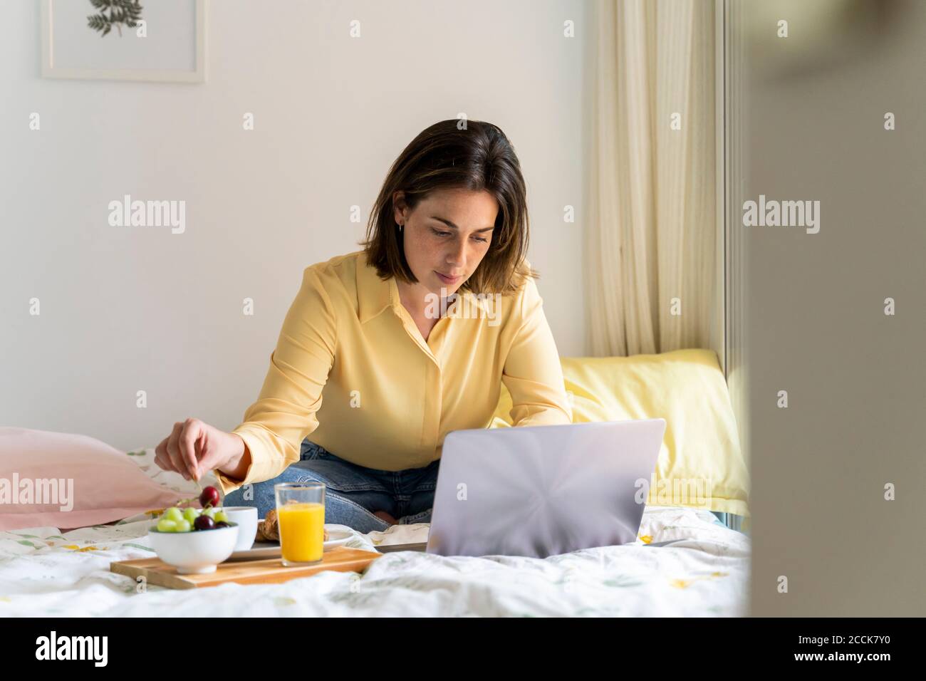 Frau beim Frühstück mit Laptop im Schlafzimmer Stockfoto