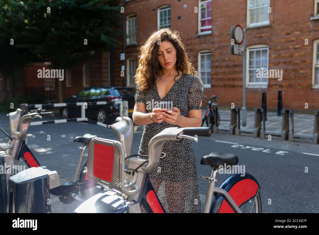 Schöne Frau, die sich ein Fahrrad über ein Smartphone am Parkplatz ausgeliehen hat Stockfoto
