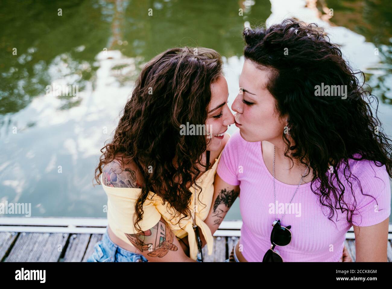 Nahaufnahme einer jungen Frau, die sich während des Sitzens auf die Nase der Freundin küsst Am See Stockfoto