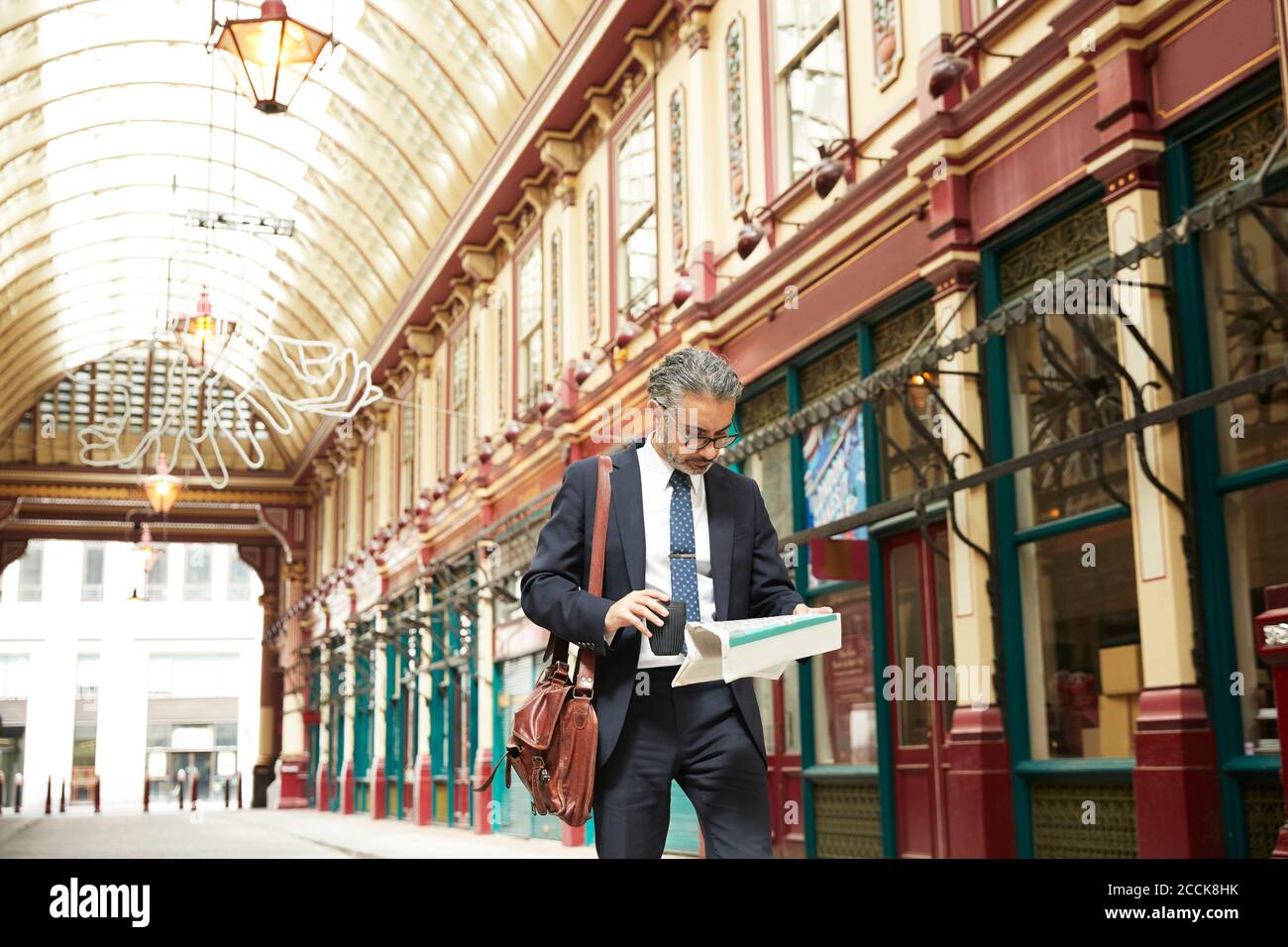 Unternehmer mit Kaffee Zeitung lesen, während in Gasse zu Fuß Stockfoto