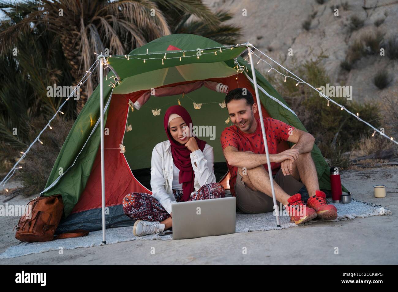 Junge Frau trägt Hijab und Mann mit Laptop an einem Zelt Stockfoto