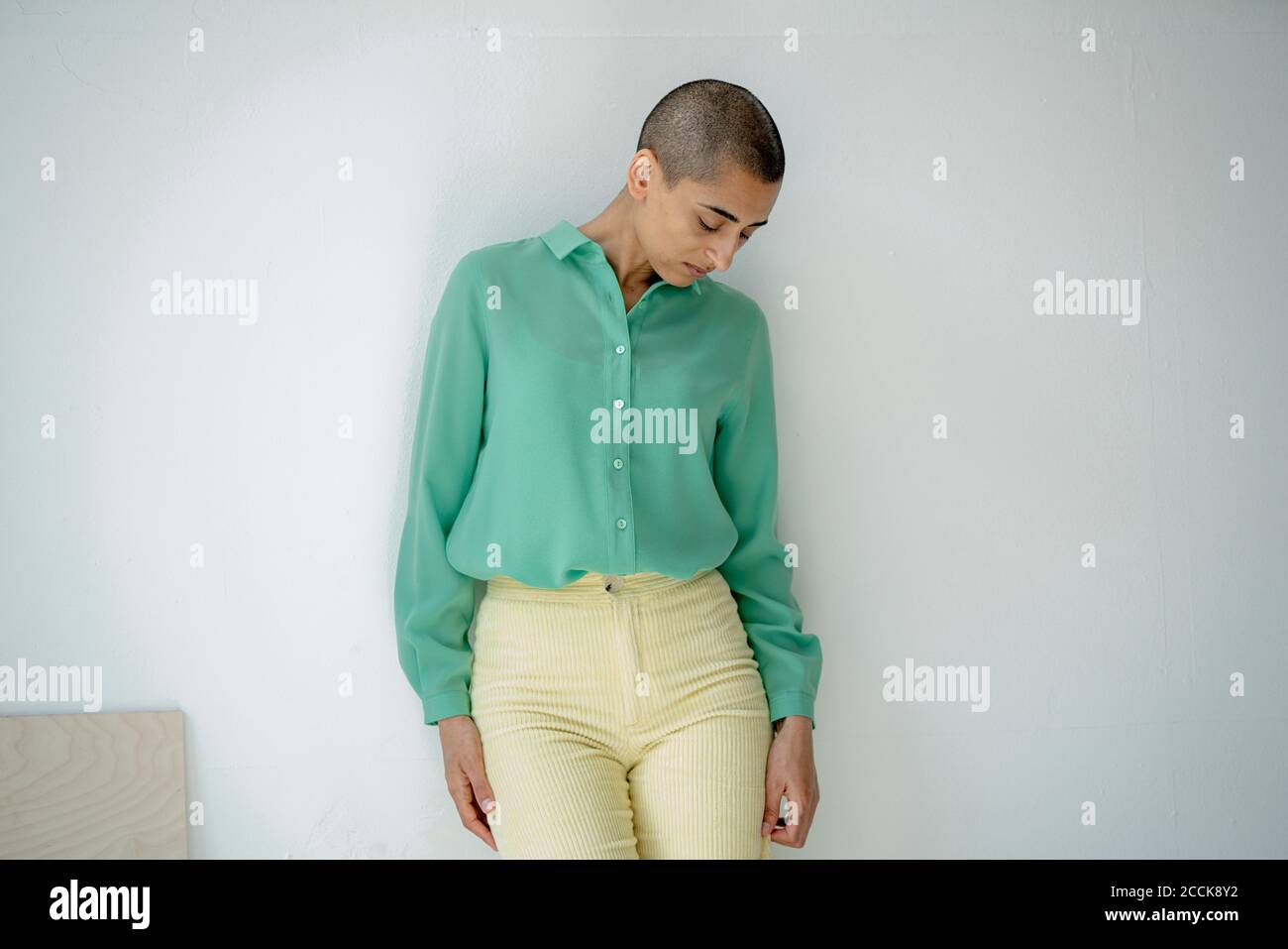 Seriöse Frau, die sich gegen eine Wand lehnt und nach unten schaut Stockfoto