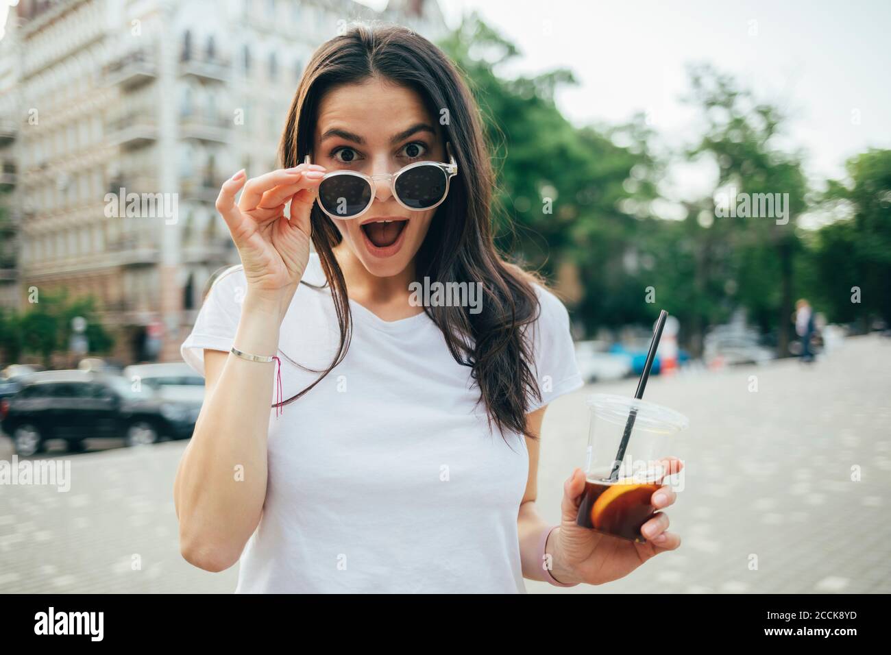 Überrascht junge Frau mit Mund offen trägt Sonnenbrille im Stehen An der City Street Stockfoto