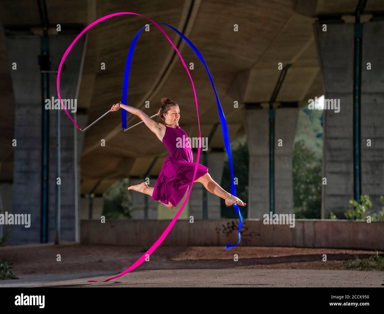 Junge Frau hält Bänder, während sie rhythmische Gymnastik unter Brücke Stockfoto