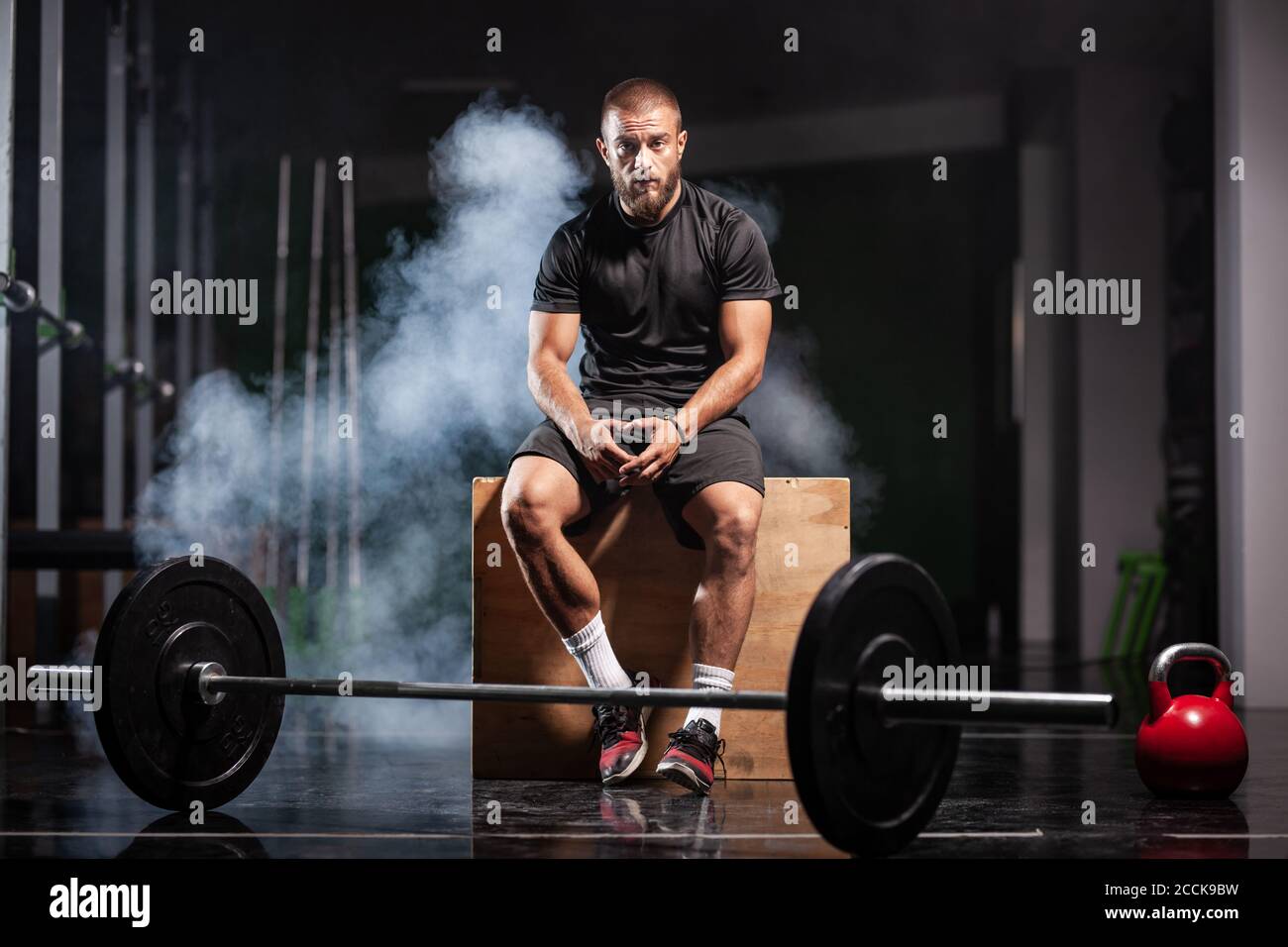 Muskulöser Sportler mit Gewichtheben Ausrüstung. CrossFit Trainer im Fitnessstudio. Rauchhintergrund. Stockfoto