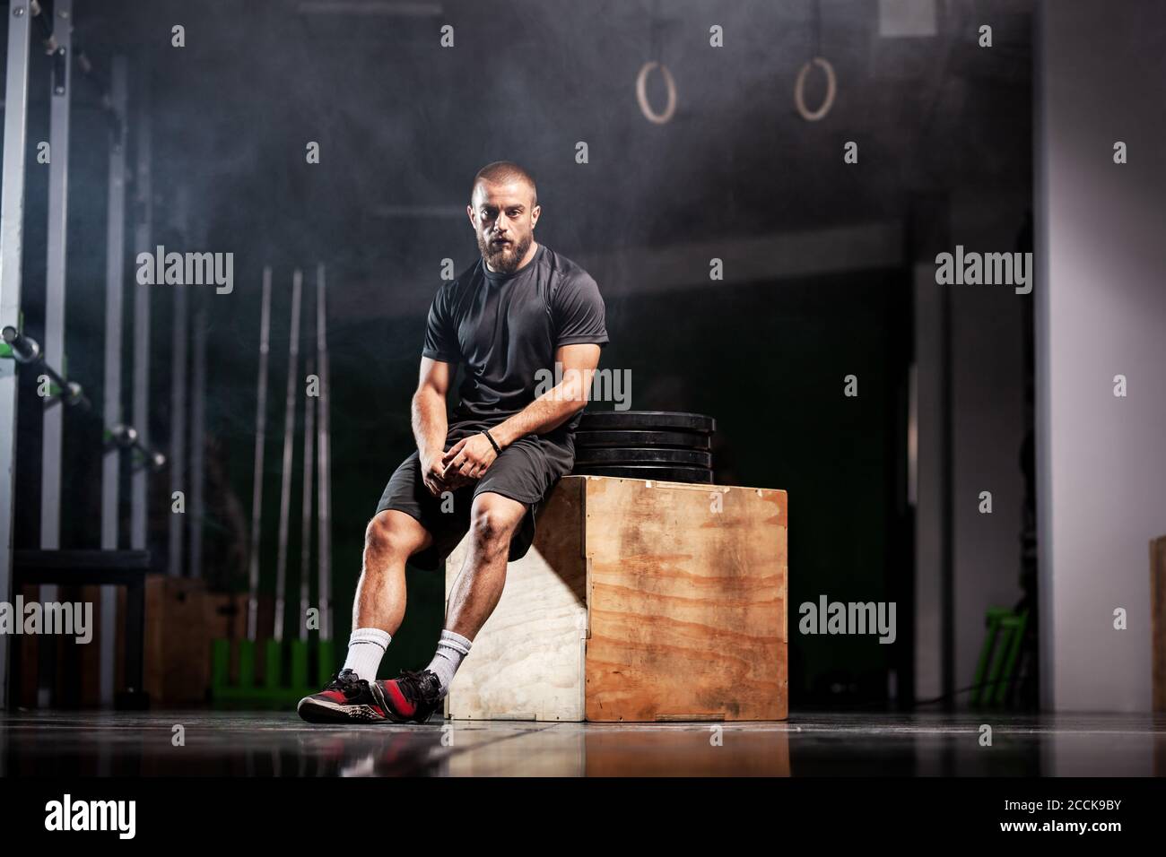 Muskulöser Sportler mit Gewichtheben Ausrüstung. CrossFit Trainer im Fitnessstudio. Rauchhintergrund. Stockfoto