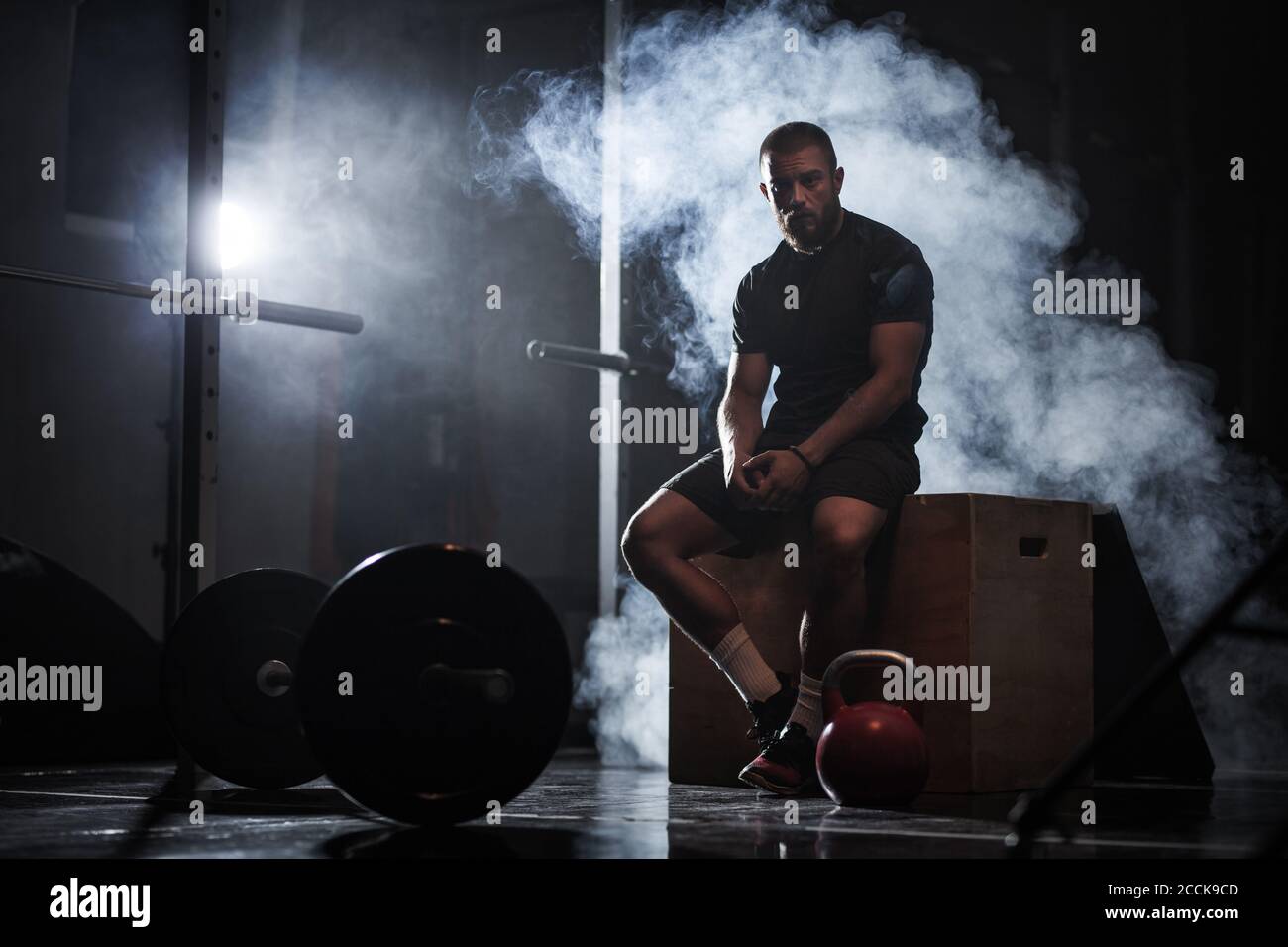 Muskulöser Sportler mit Gewichtheben Ausrüstung. CrossFit Trainer im Fitnessstudio. Rauchhintergrund. Stockfoto