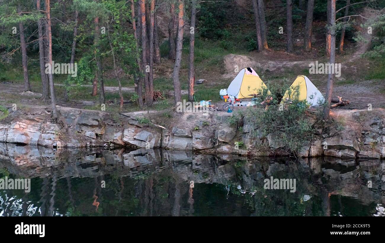 Schöne Landschaft, Camping und Zelte unter dem Pinienwald am Rande des überfluteten Granitsteinbruchs Stockfoto