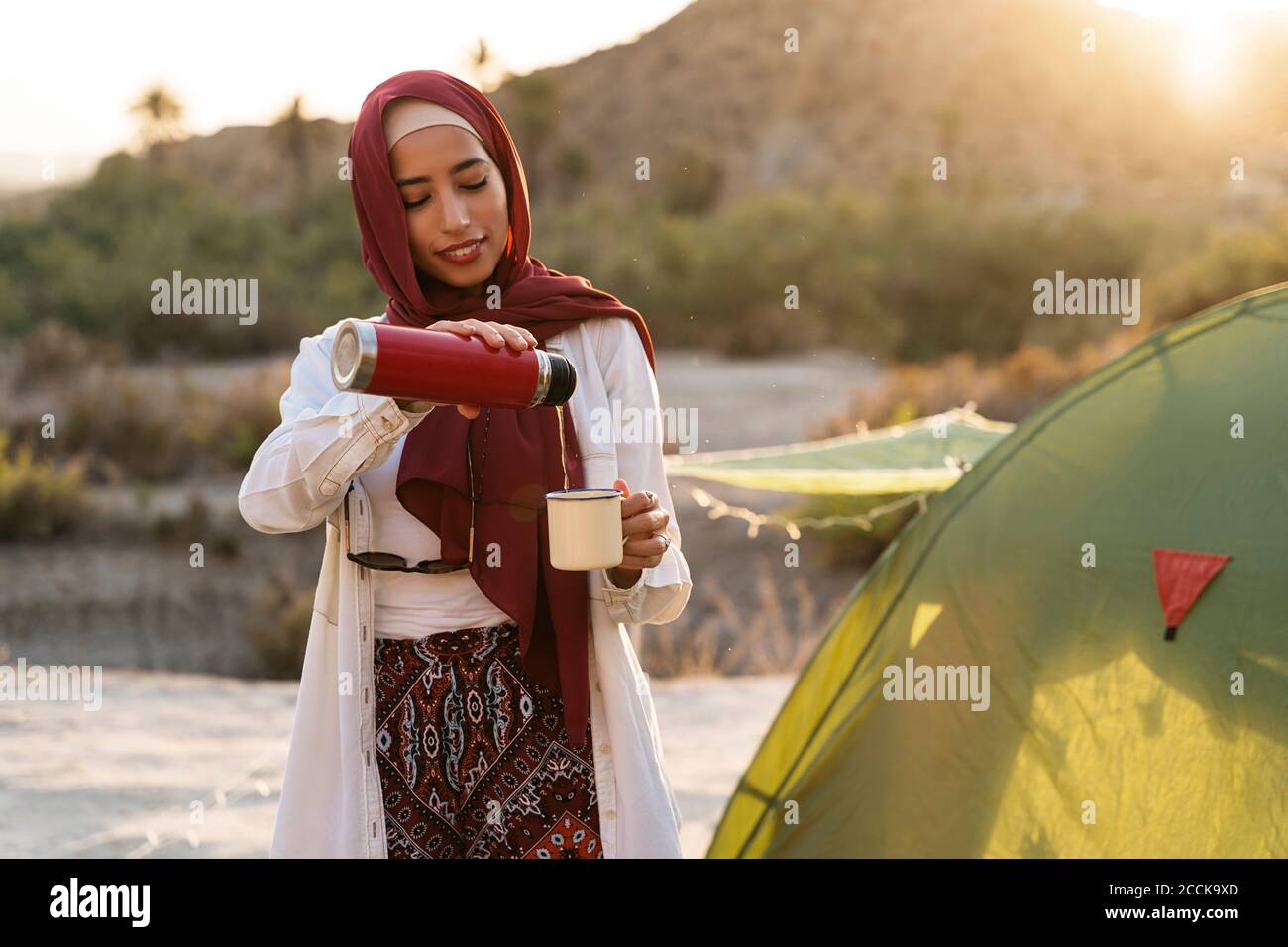 Lächelnd junge Touristen Frau trägt Hijab an einem Zelt Gießen Tee in Becher Stockfoto