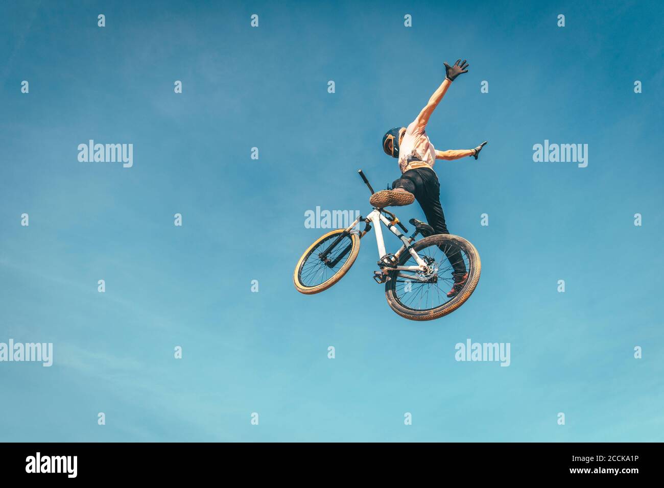 Sorgloser Mann mit Fahrrad gegen blauen Himmel während Stunt durchführen Sonnenuntergang Stockfoto