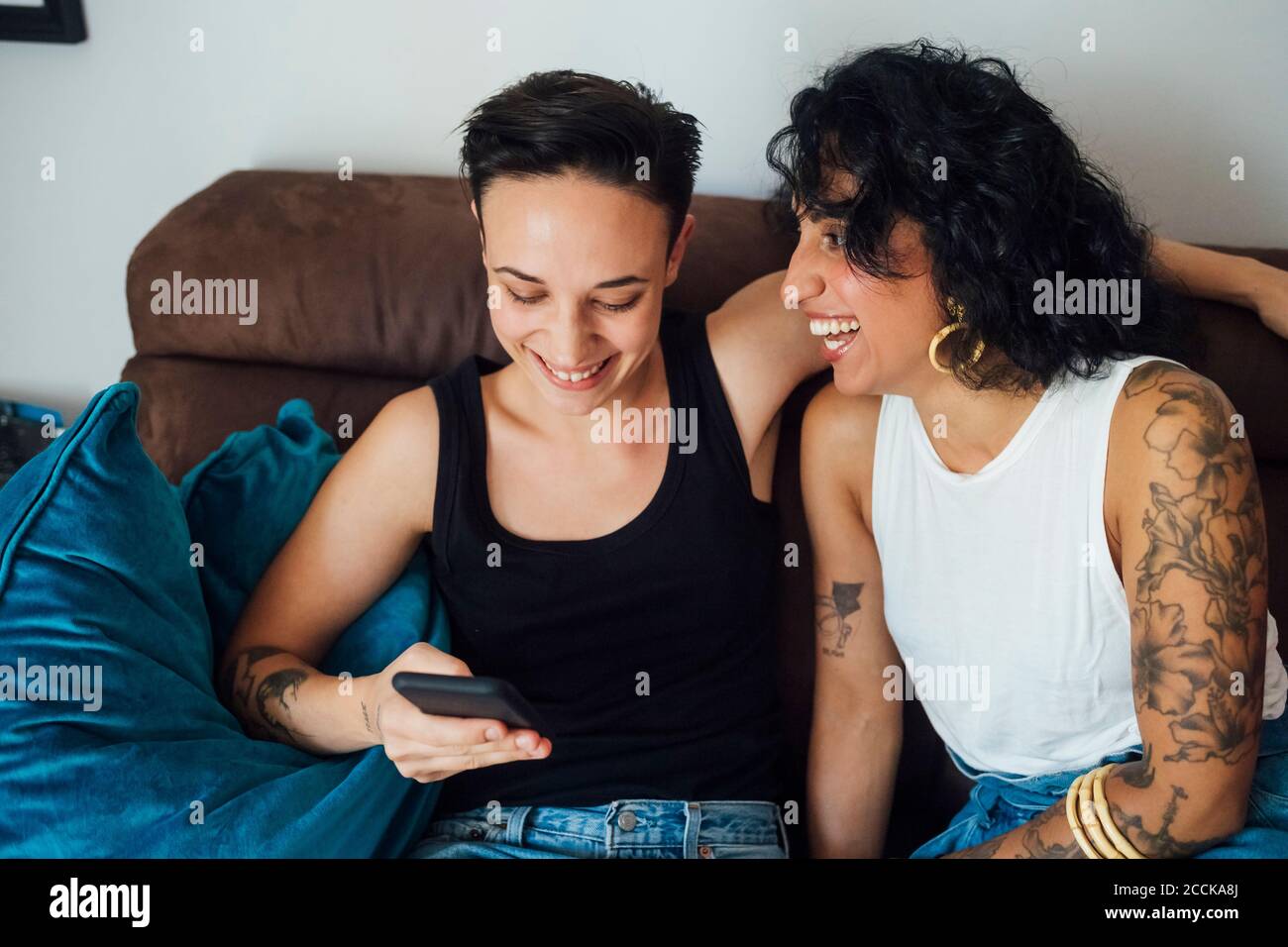 Fröhliche Frau, die den Partner mit dem Telefon auf dem Sofa ansieht Stockfoto