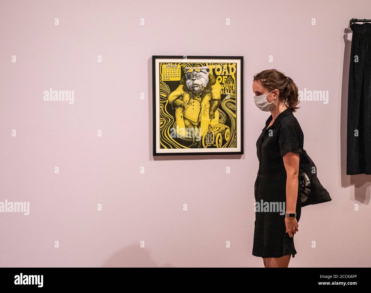 Eine Frau mit Gesichtsbedeckung und schwarzem Kleid steht an einer gelben Zeichnung von Aubrey Beardsley. Stockfoto