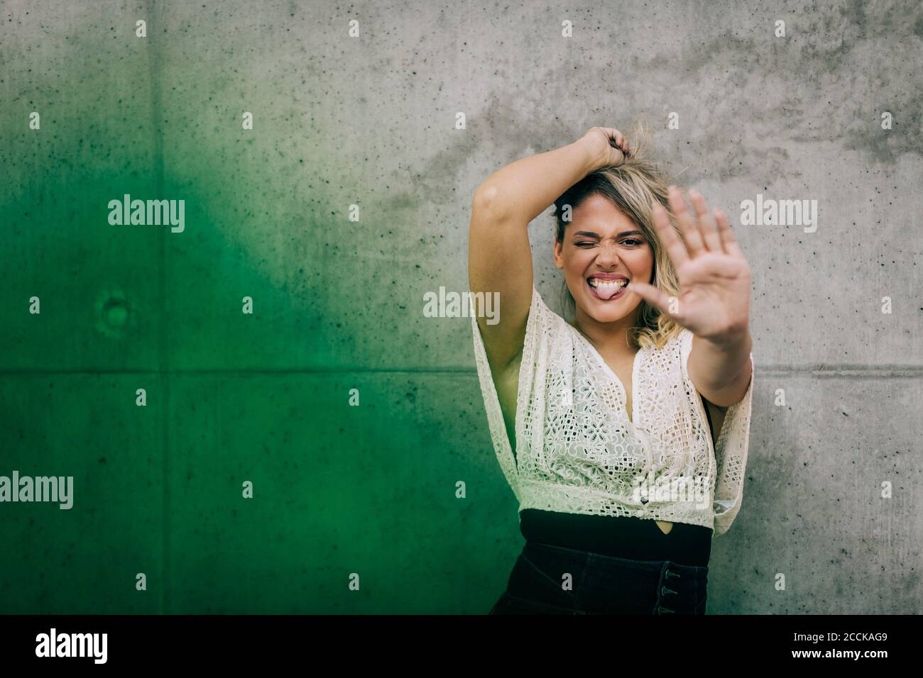 Junge Frau mit Stop-Geste, während sie gegen die grüne Wand steht Stockfoto