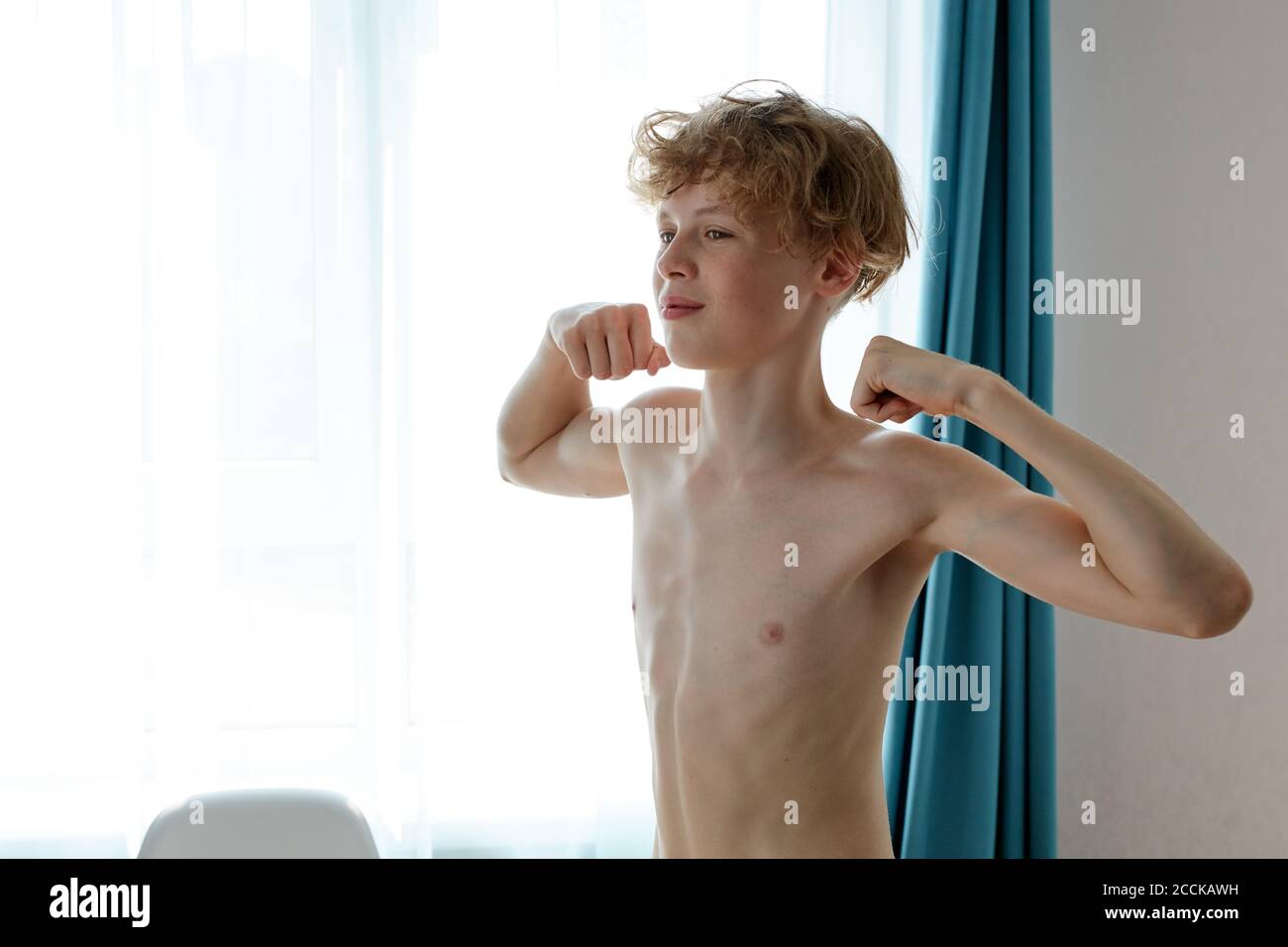 Junge kaukasische Teenager Junge zeigt Arme Muskeln, stolz. Fitness-Konzept. Zu Hause Stockfoto