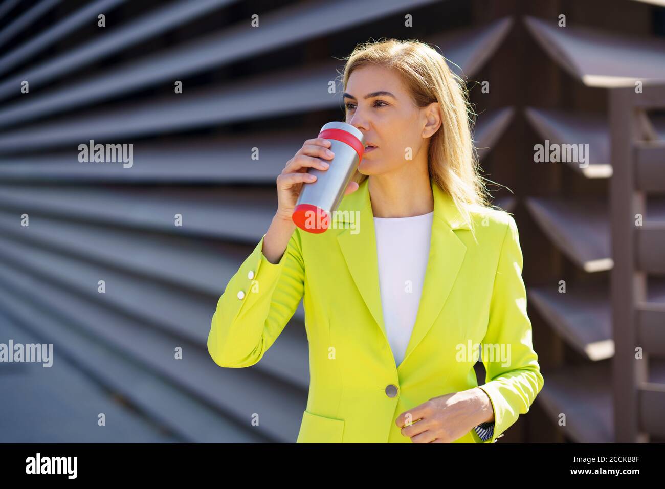 Reife Geschäftsfrau trinkt Kaffee aus Reisebecher beim Stehen gegen Geländer Stockfoto