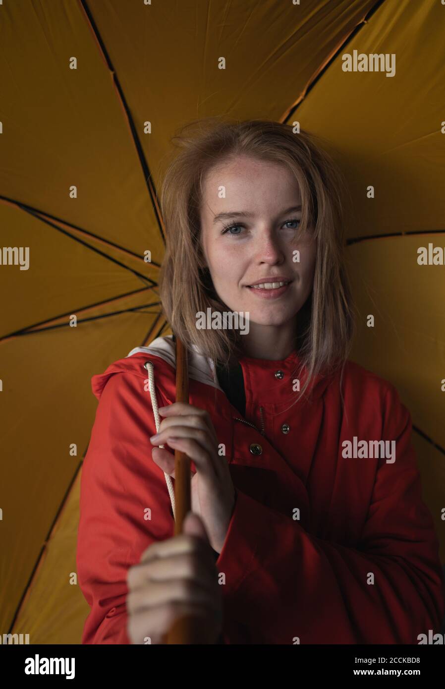 Nahaufnahme einer Frau mit blonden Haaren, die den gelben Regenschirm im Stehen hält In der Stadt Stockfoto