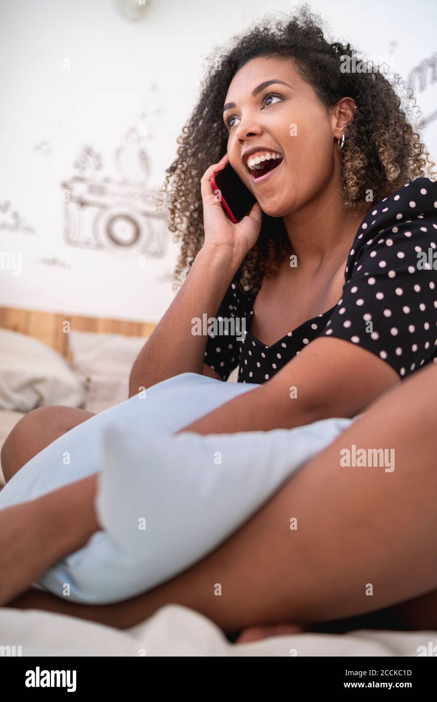 Frau mit offenem Mund spricht über Smartphone, während sie sitzt Auf dem Bett zu Hause Stockfoto