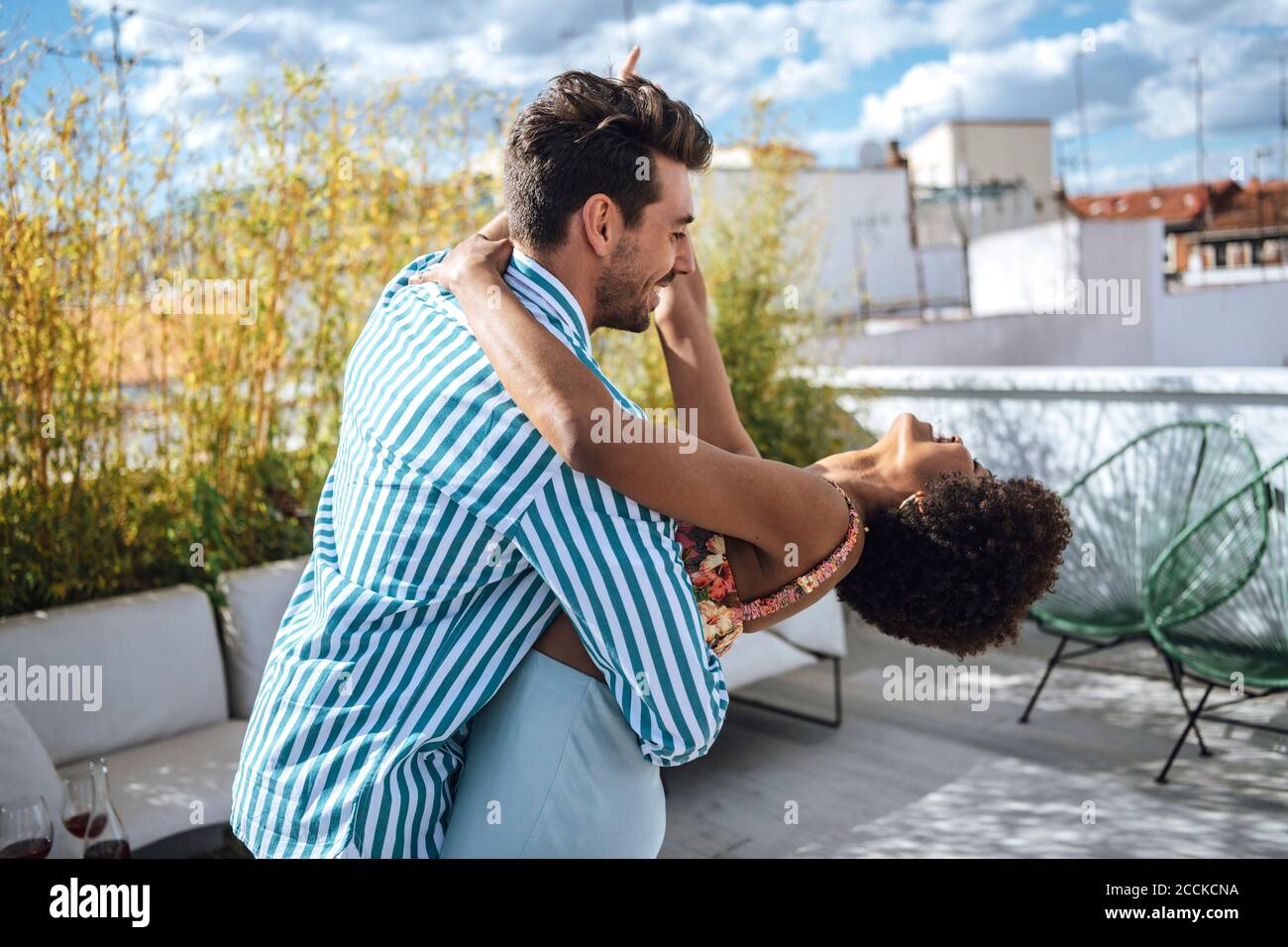 Fröhliches multiethnisches Paar, das an sonnigen Tagen auf der Penthouse-Terrasse tanzt Stockfoto