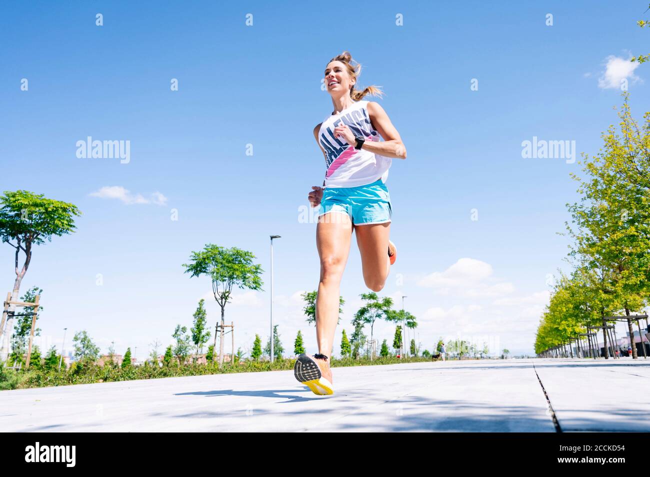 Mittlere Erwachsene Frau, die auf der Straße gegen den blauen Himmel joggt Stockfoto