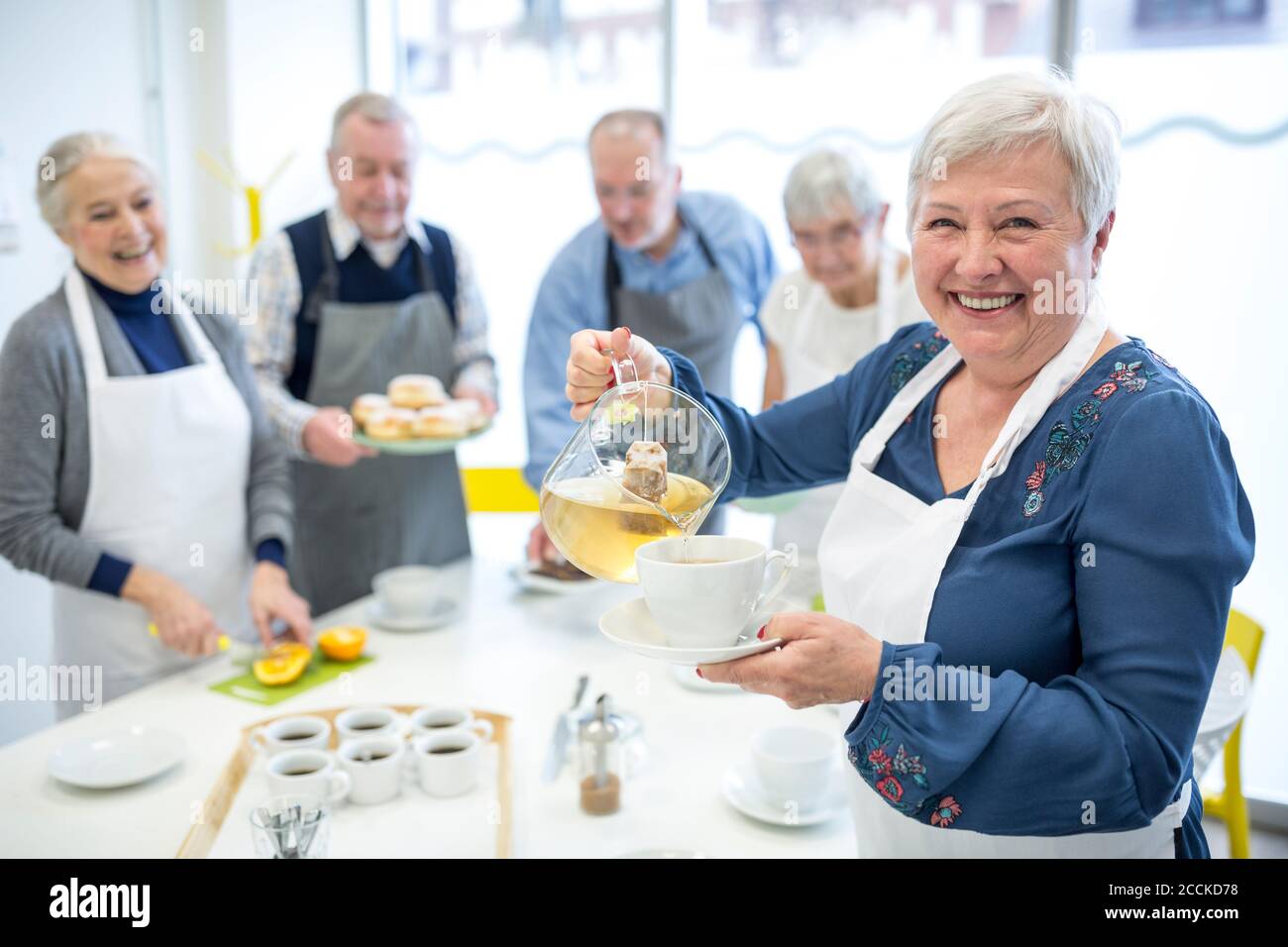 Ältere Frau gießt Tee in der Tasse für Kaffee Party in Altersheim Stockfoto