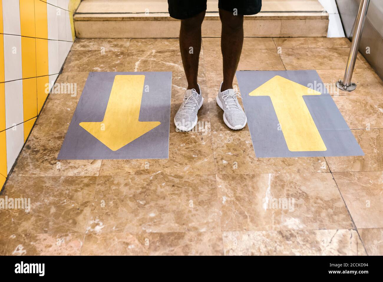 Beine von jungen Mann stehen durch Pfeil Symbole auf dem Boden An der U-Bahn-Station Stockfoto