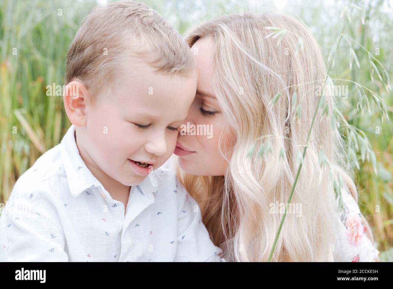 Nahaufnahme der jungen Frau küssen niedlichen Sohn, während im Sitzen Haferfeld Stockfoto