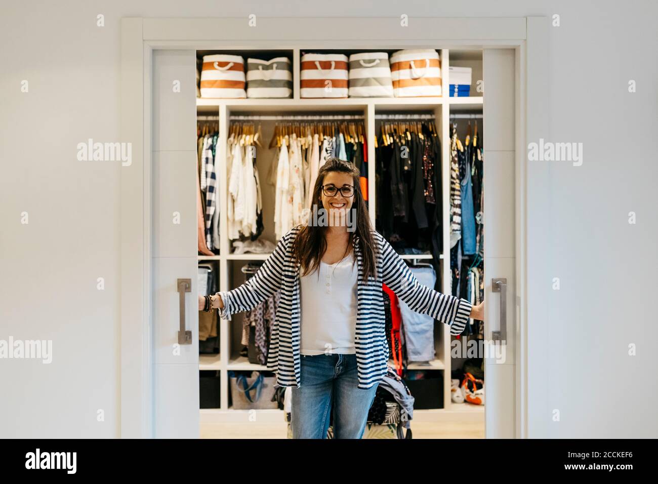 Lächelnde Frau, die die Türen des Ankleidezimmers zu Hause öffnete Stockfoto