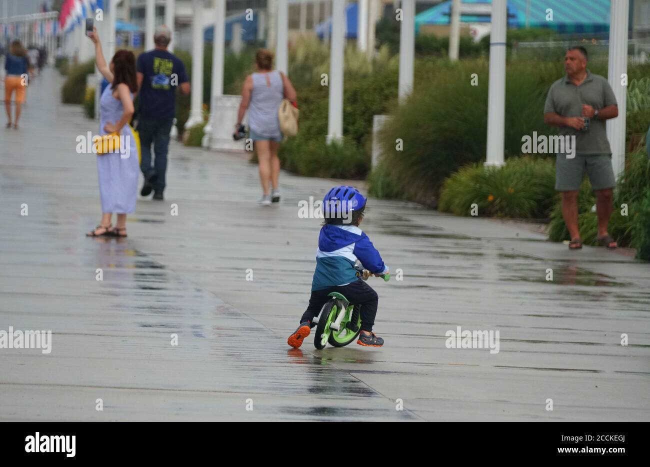 Virginia Beach, USA - 29. Juni 2020 - EIN kleiner Junge, der an einem nassen Sommertag auf dem Boardwalk mit dem Fahrrad fährt Stockfoto