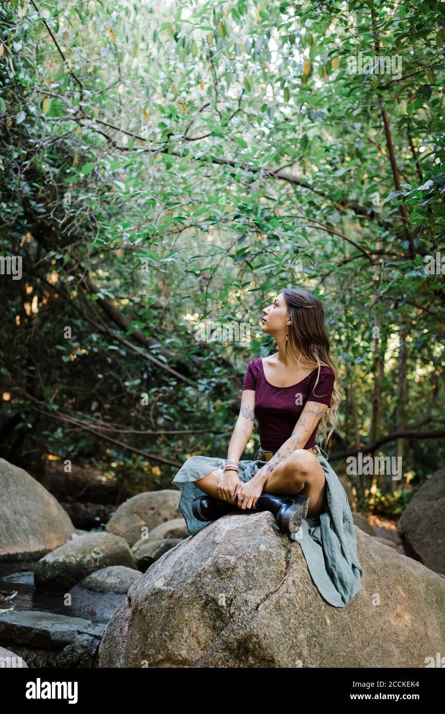 Junge Frau, die im Park auf Stein sitzt Stockfoto