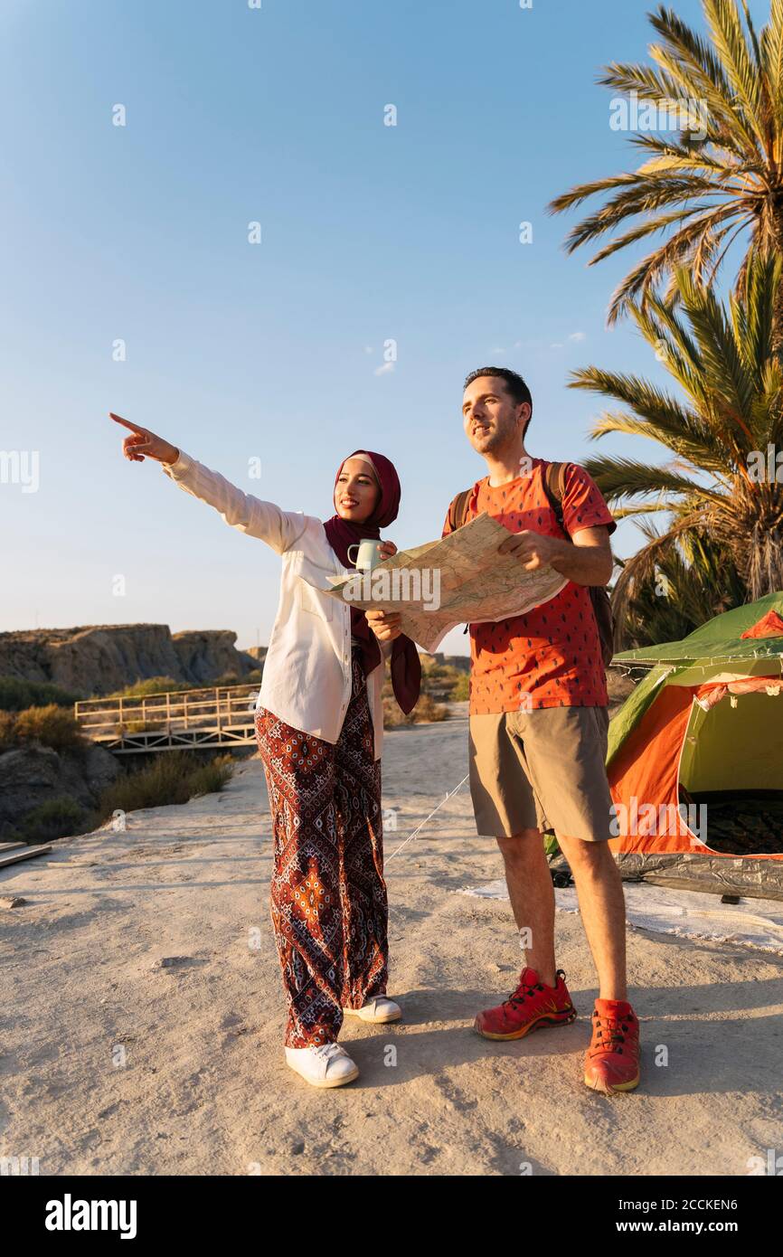 Junge Frau trägt Hijab an einem Zelt, das den Weg zeigt An den Mann, der eine Karte hält Stockfoto