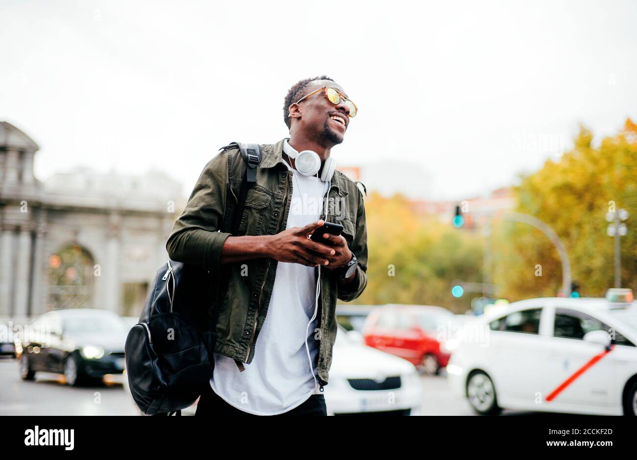Glücklicher Mann mit Sonnenbrille und Smartphone, während er sich dagegen aufhält Himmel in der Stadt Stockfoto