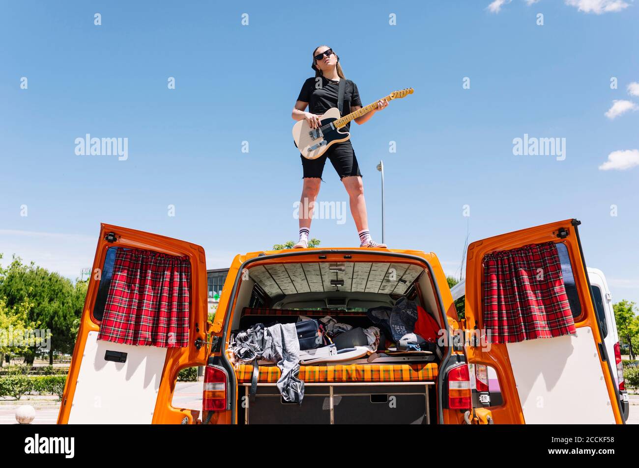 Junge Frau spielt Gitarre, steht auf offenem Van Stockfoto