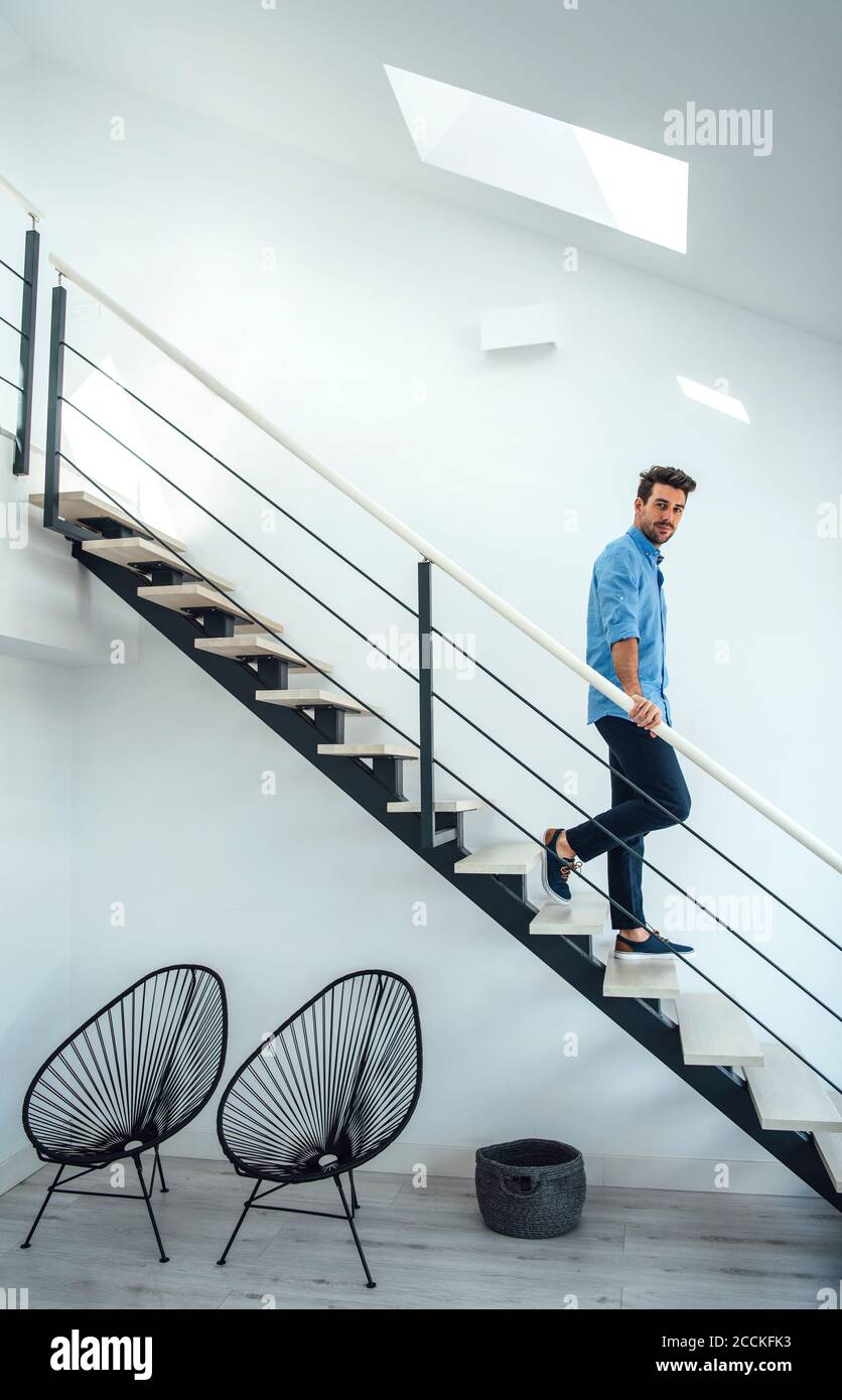 Mittelerwachsener Mann, der sich im modernen Penthouse die schwimmende Treppe hinunter bewegt Stockfoto