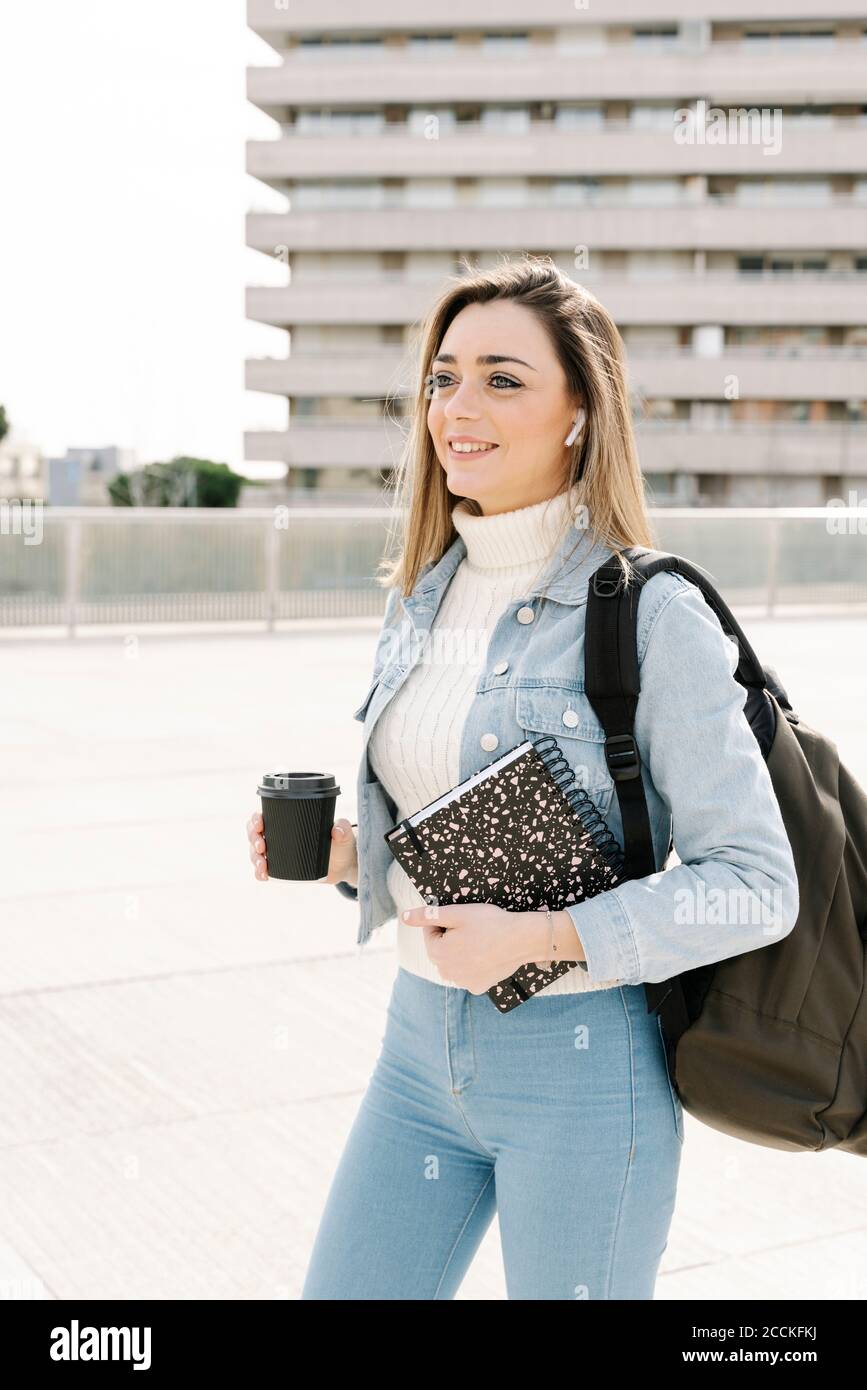 Lächelnder Student mit Kaffee und Buch auf dem Universitätscampus Stockfoto