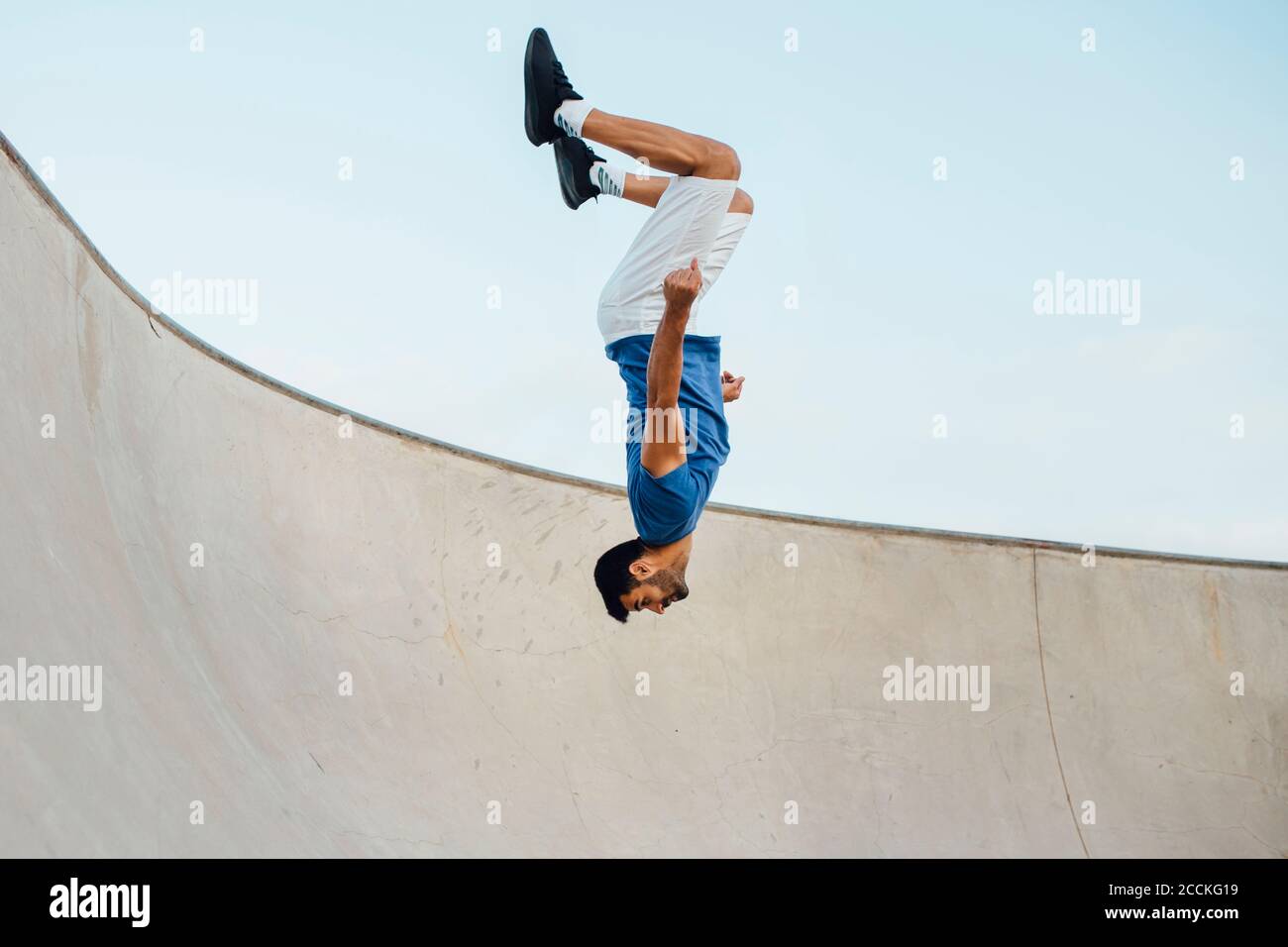 Auf dem Kopf des jungen Mannes, der Wallflip auf der Sportrampe macht Gegen den Himmel Stockfoto