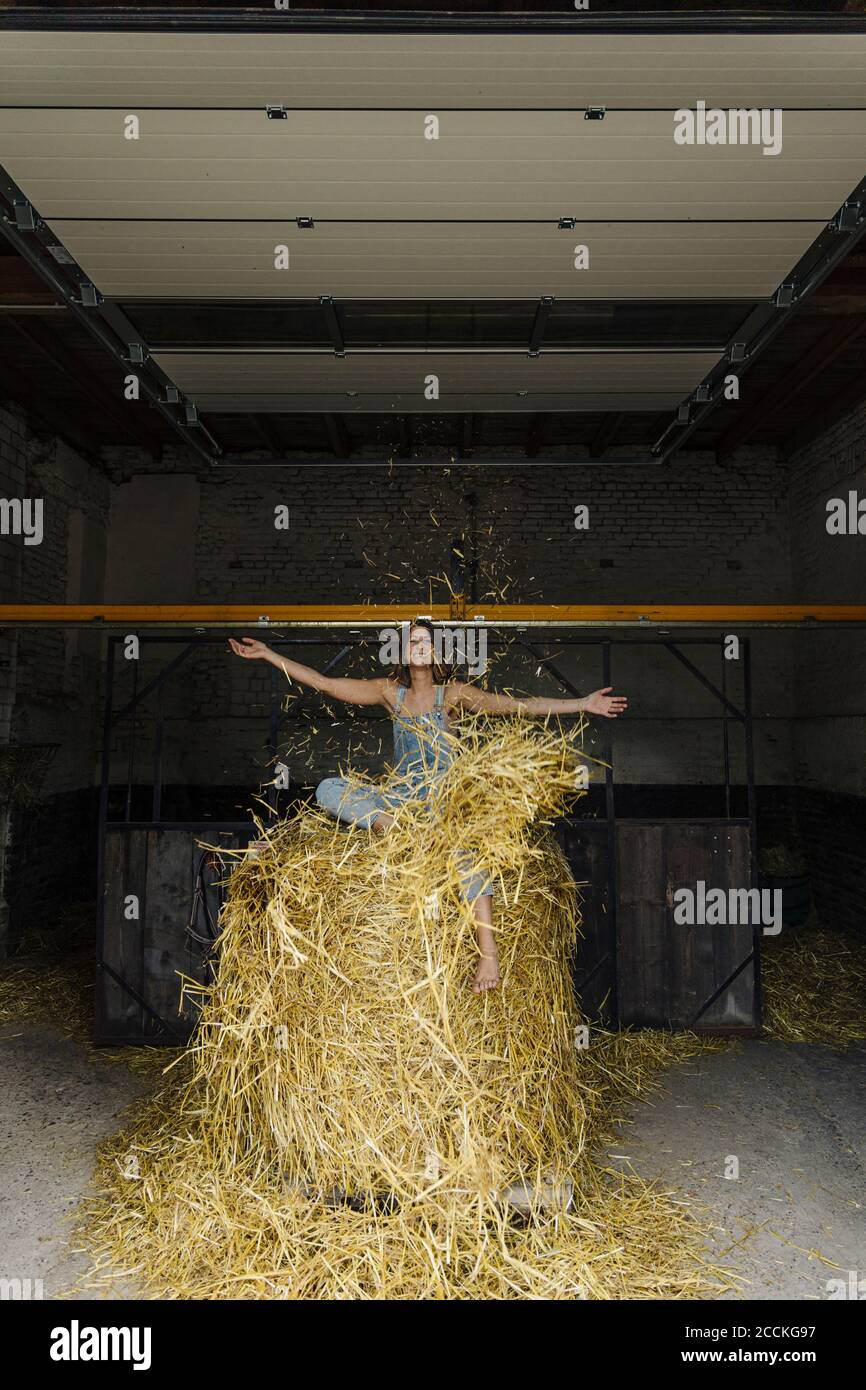 Carefrre junge Frau sitzt auf Stroh in einer Scheune auf Eine Farm Stockfoto