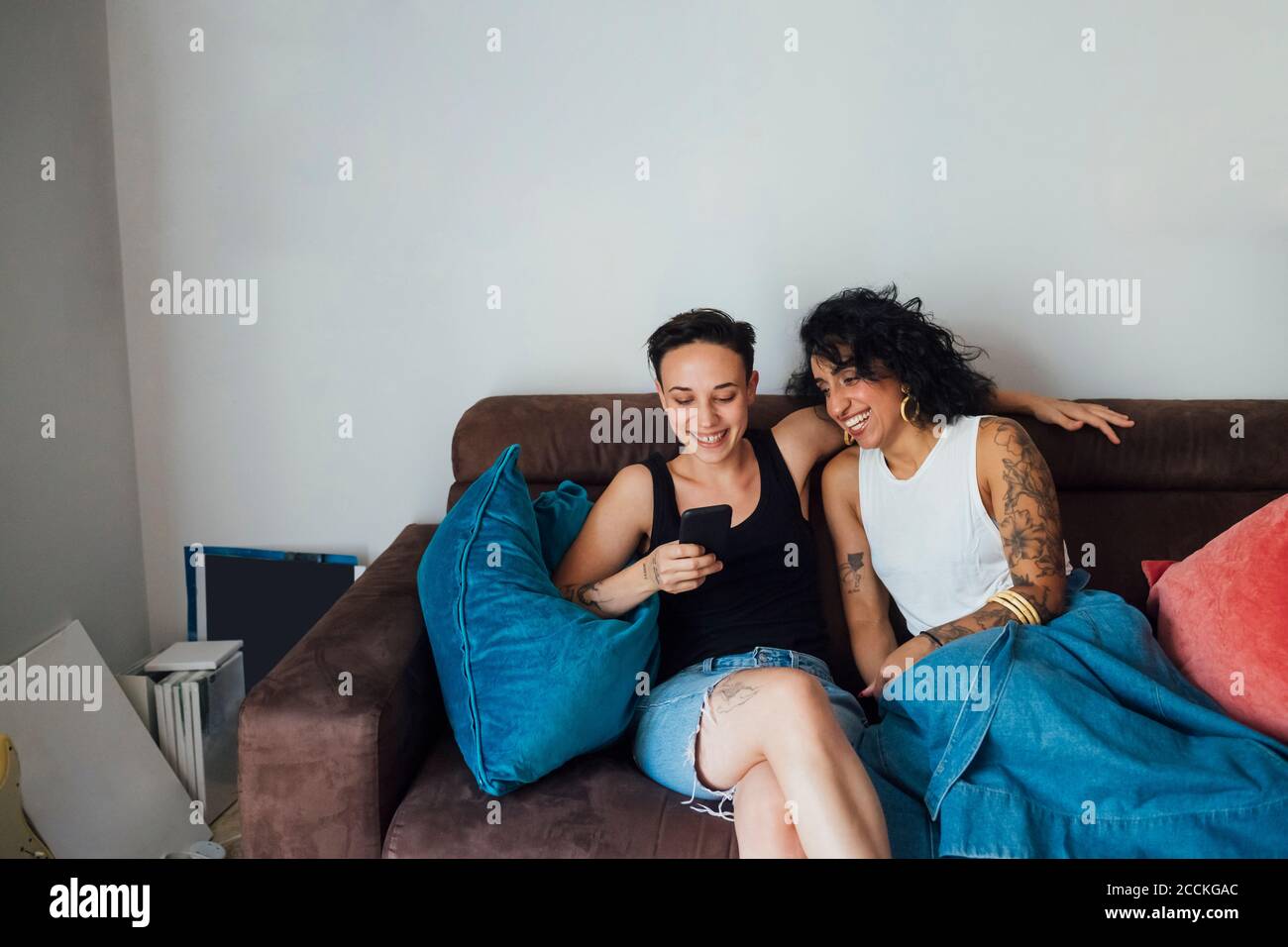 Fröhliches Paar, das Telefon benutzt, während es auf dem Sofa sitzt Stockfoto