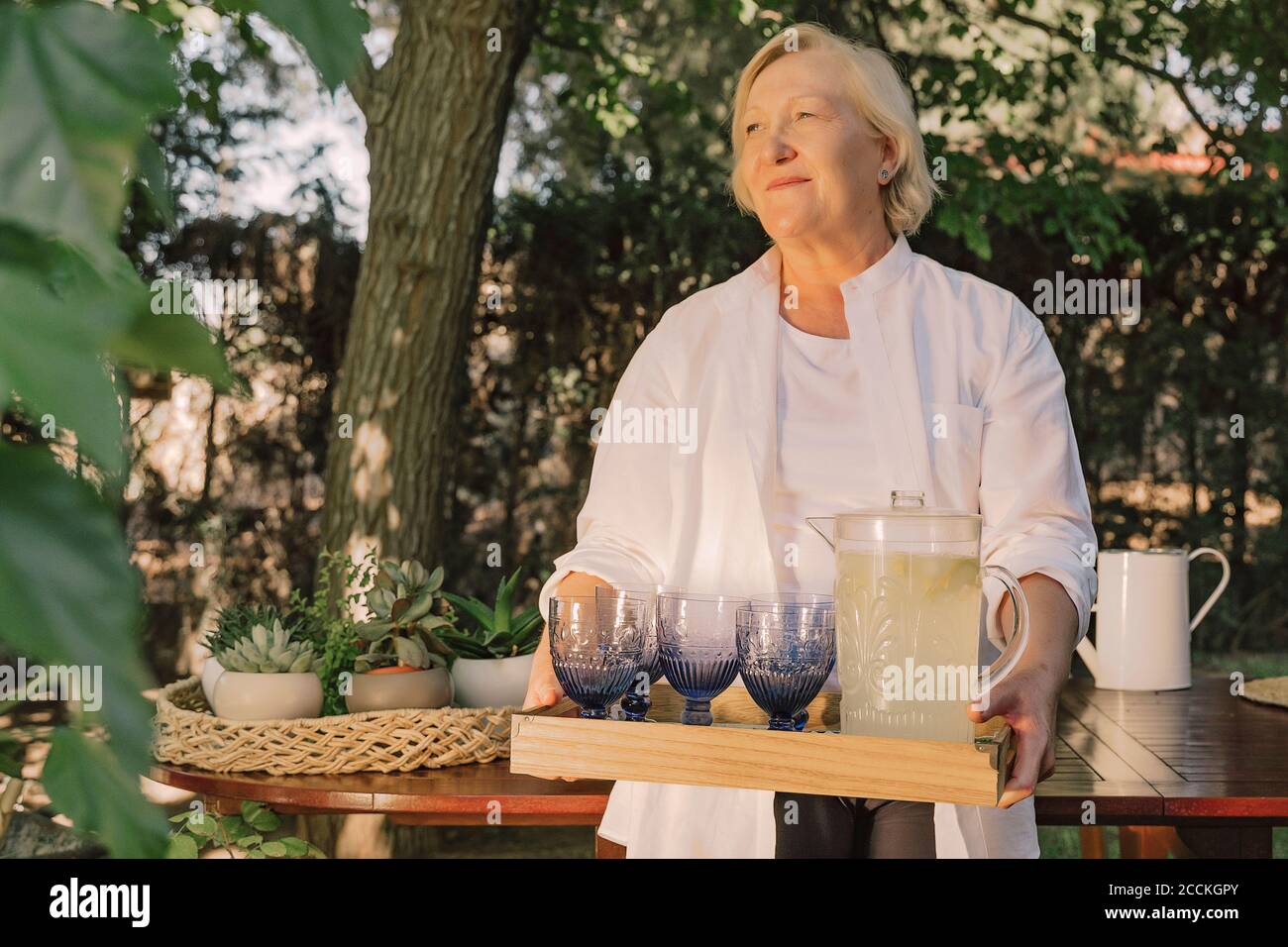 Nachdenkliche ältere Frau, die Tablett mit Getränken trug, während sie im Stehen stand Hof Stockfoto