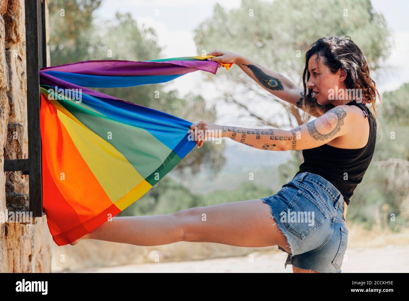 Mittlere Erwachsene Frau hält Regenbogenfahne, während sie bei Stein steht Wand Stockfoto