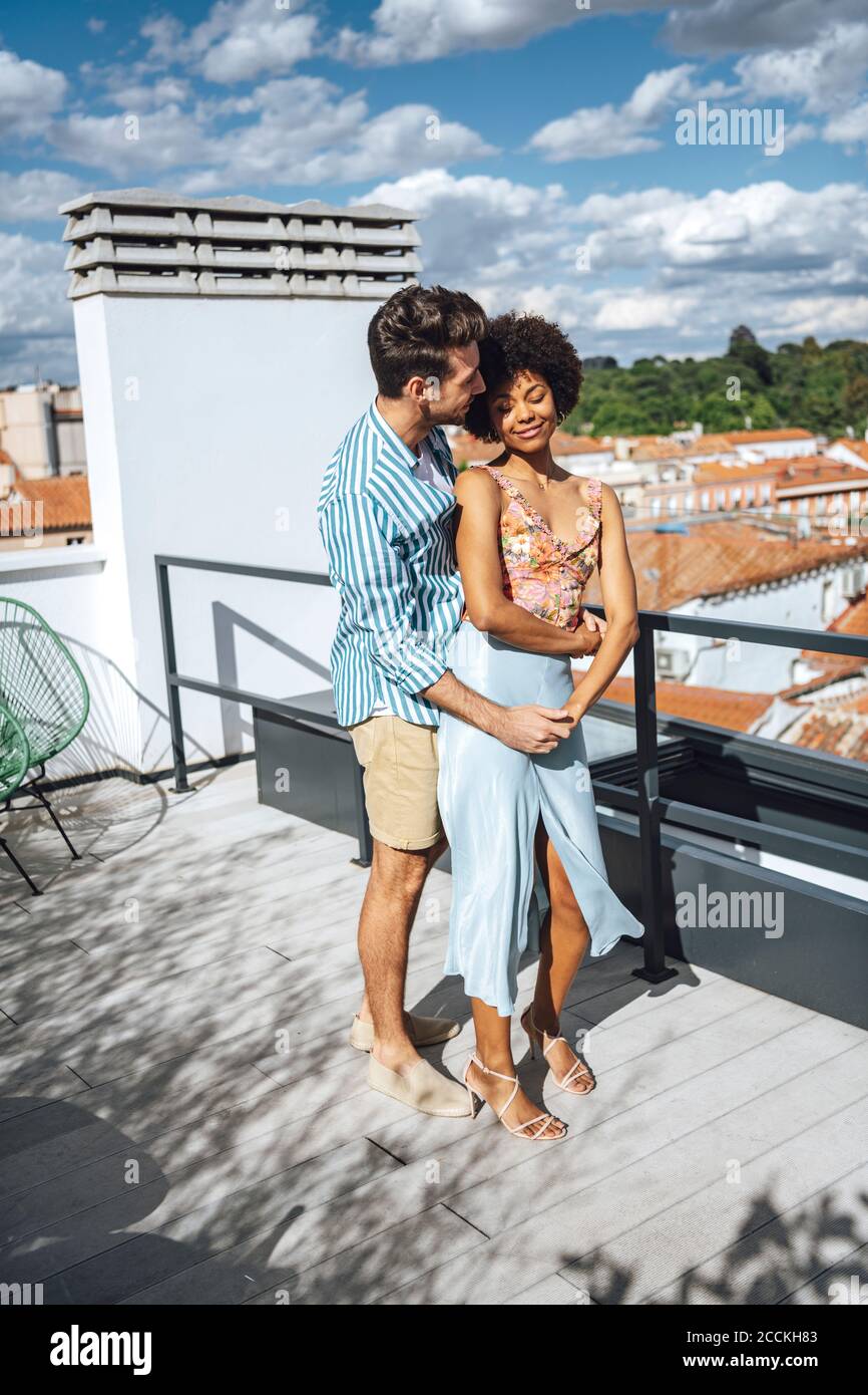 Romantisches multi-ethnisches Paar umarmt auf Penthouse Terrasse während sonnigen Tag Stockfoto