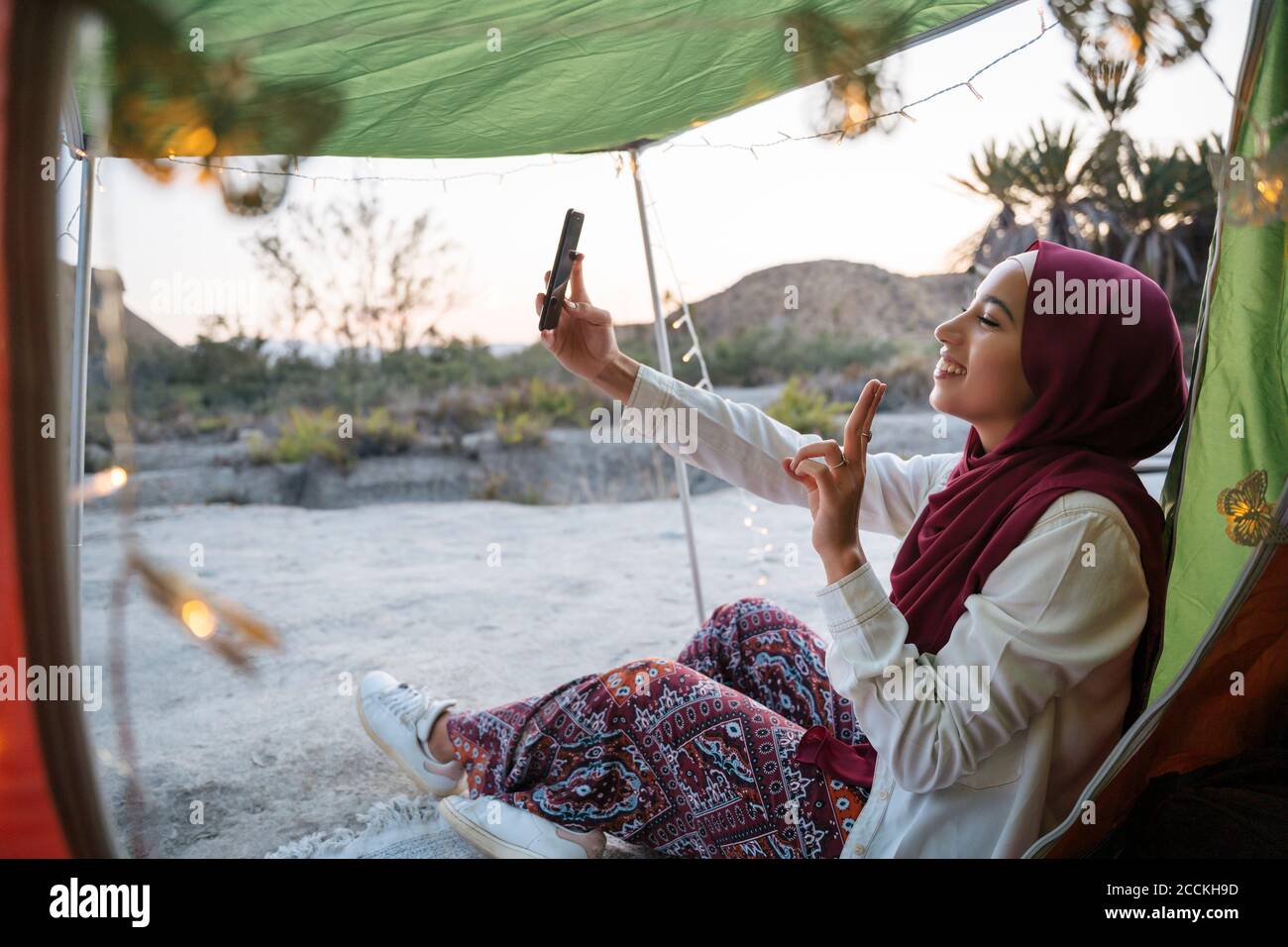 Glückliche junge Touristenfrau trägt Hijab bei einem Zeltplatz Ein Selfie Stockfoto